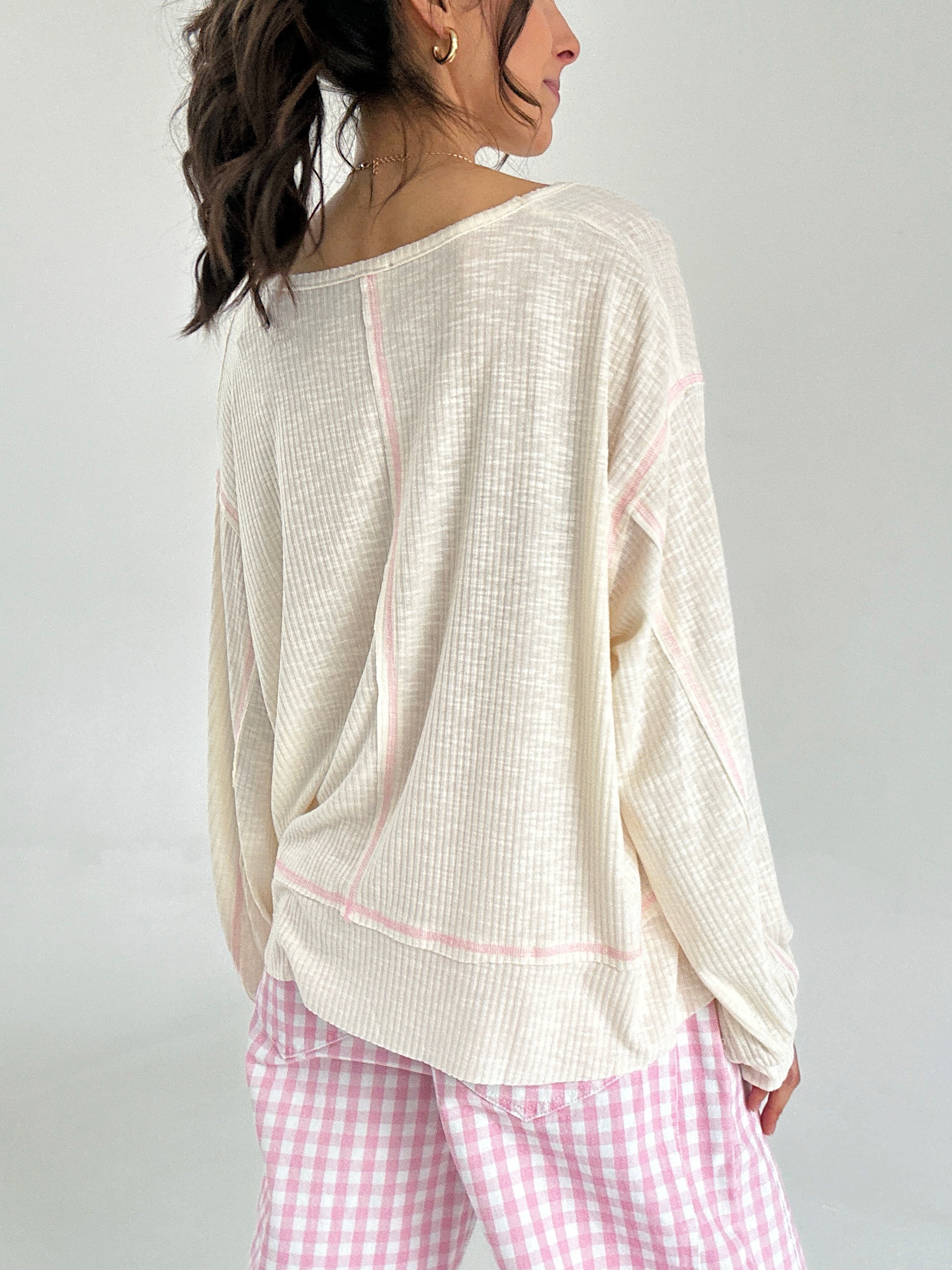 Woman wearing a beige long-sleeve top and pink checkered pants on a plain background from back