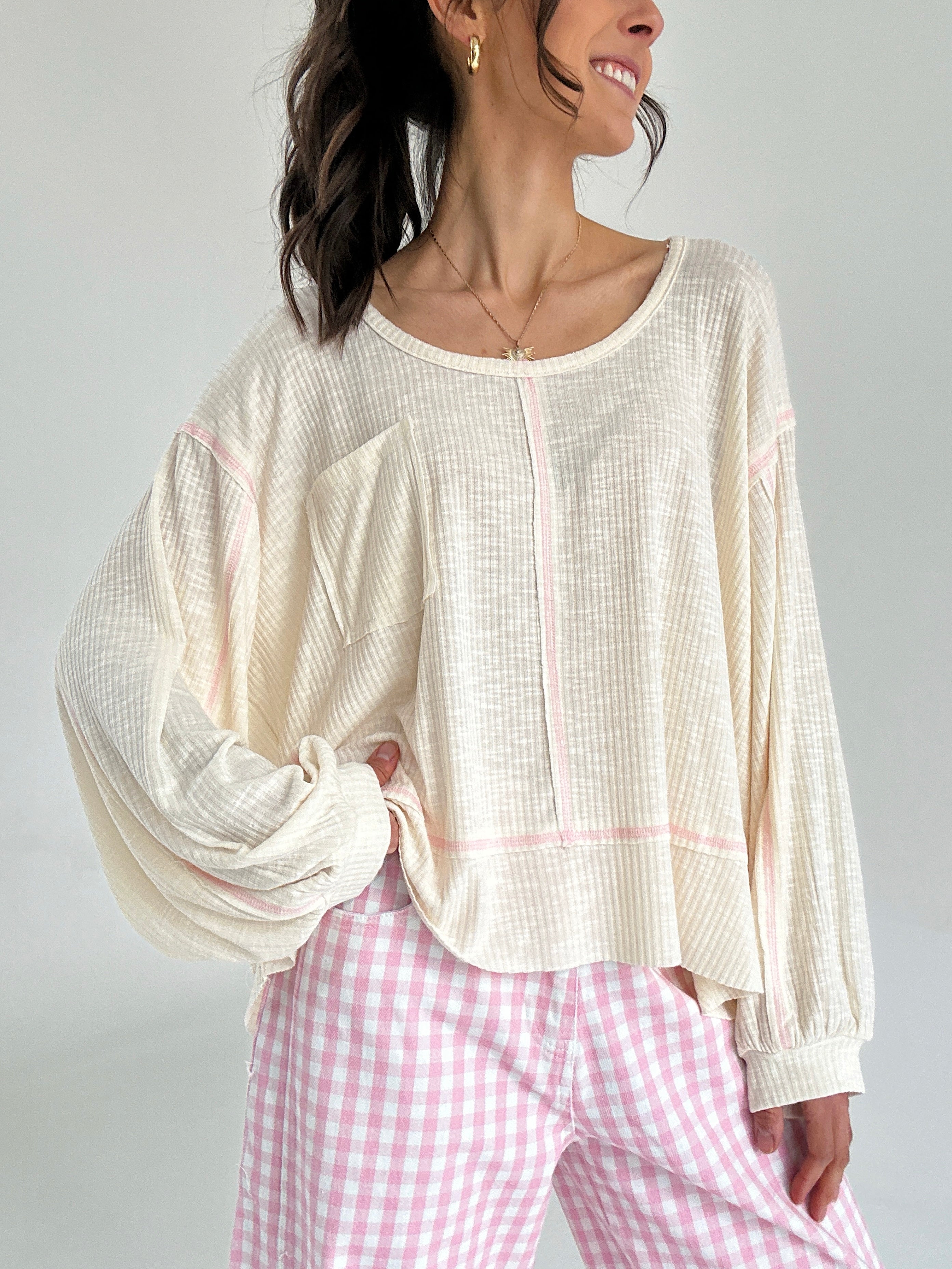 Woman wearing a cream-colored top and pink checkered pants on a plain background