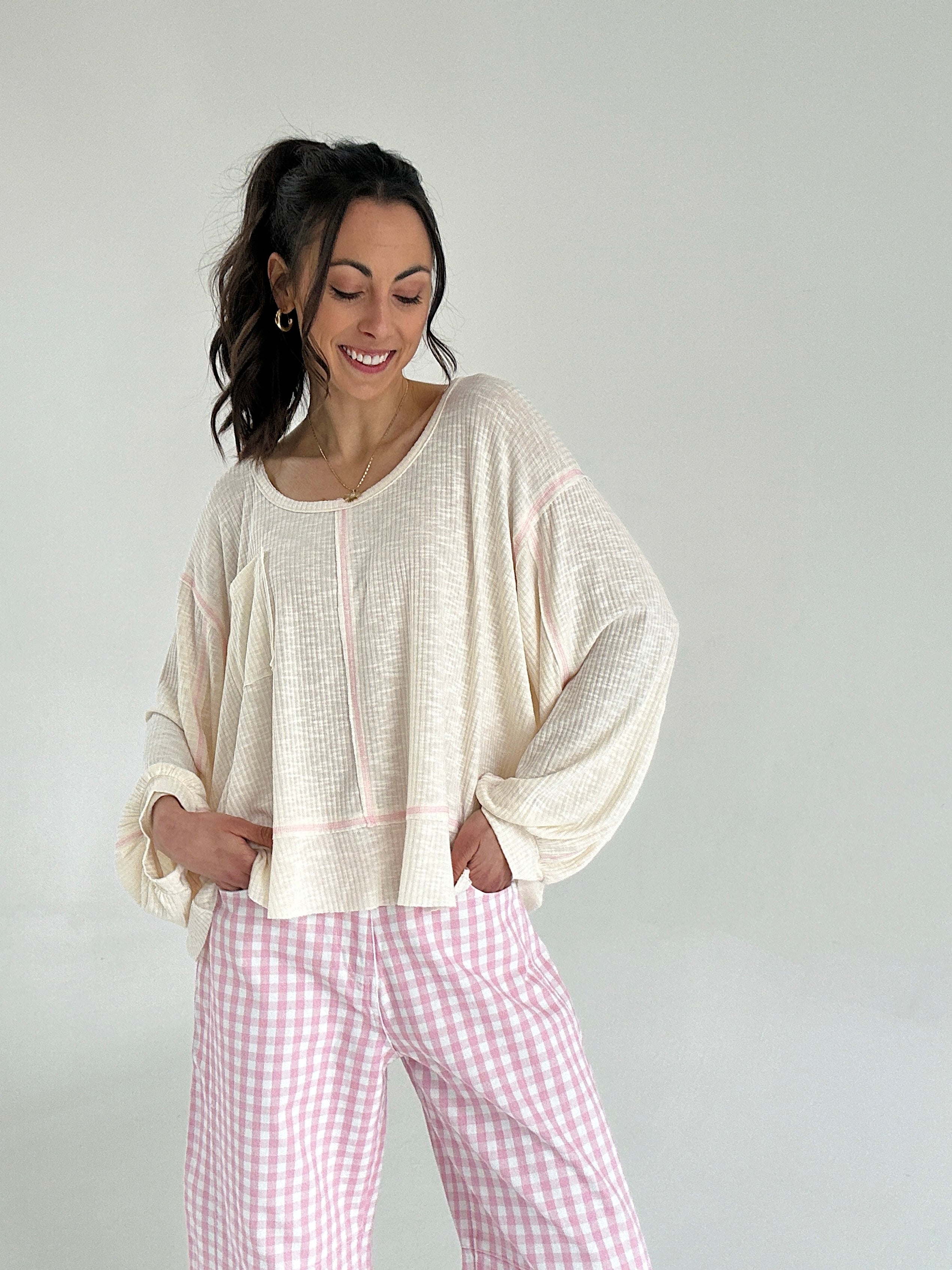 Woman wearing a cream top and pink checkered pants against a white background