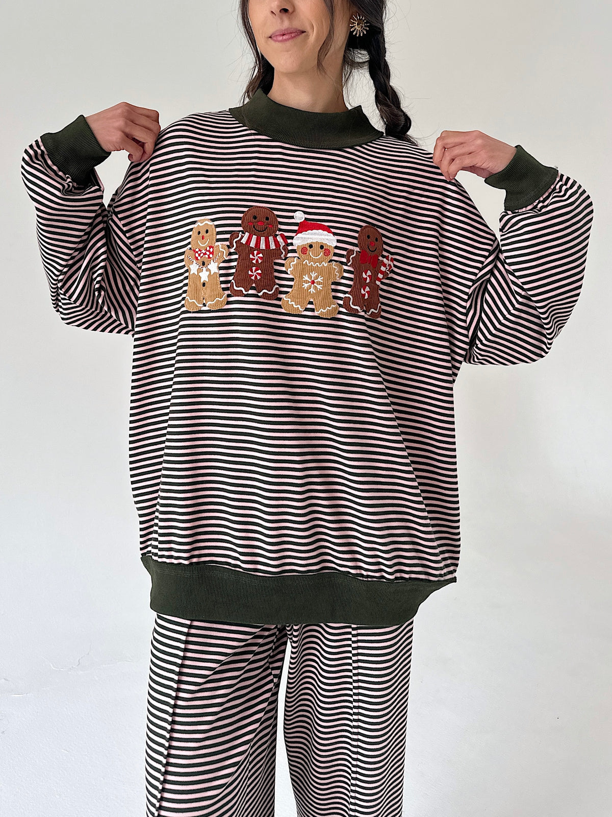 A woman wearing a matching holiday pajama set with horizontal stripes, dark green ribbed trim, and a gingerbread-themed graphic on the front.