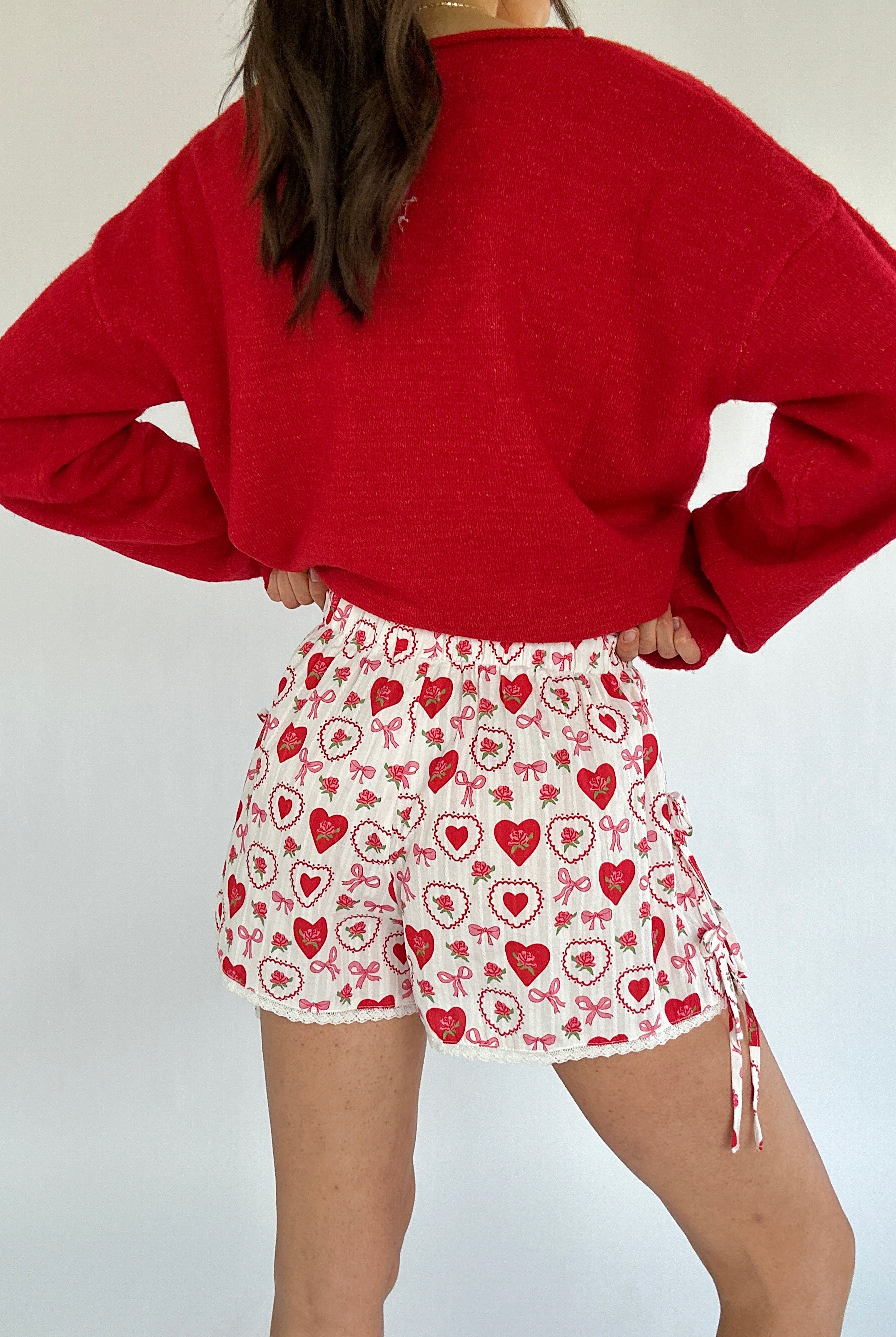 Person wearing a red sweater and patterned shorts on a plain background