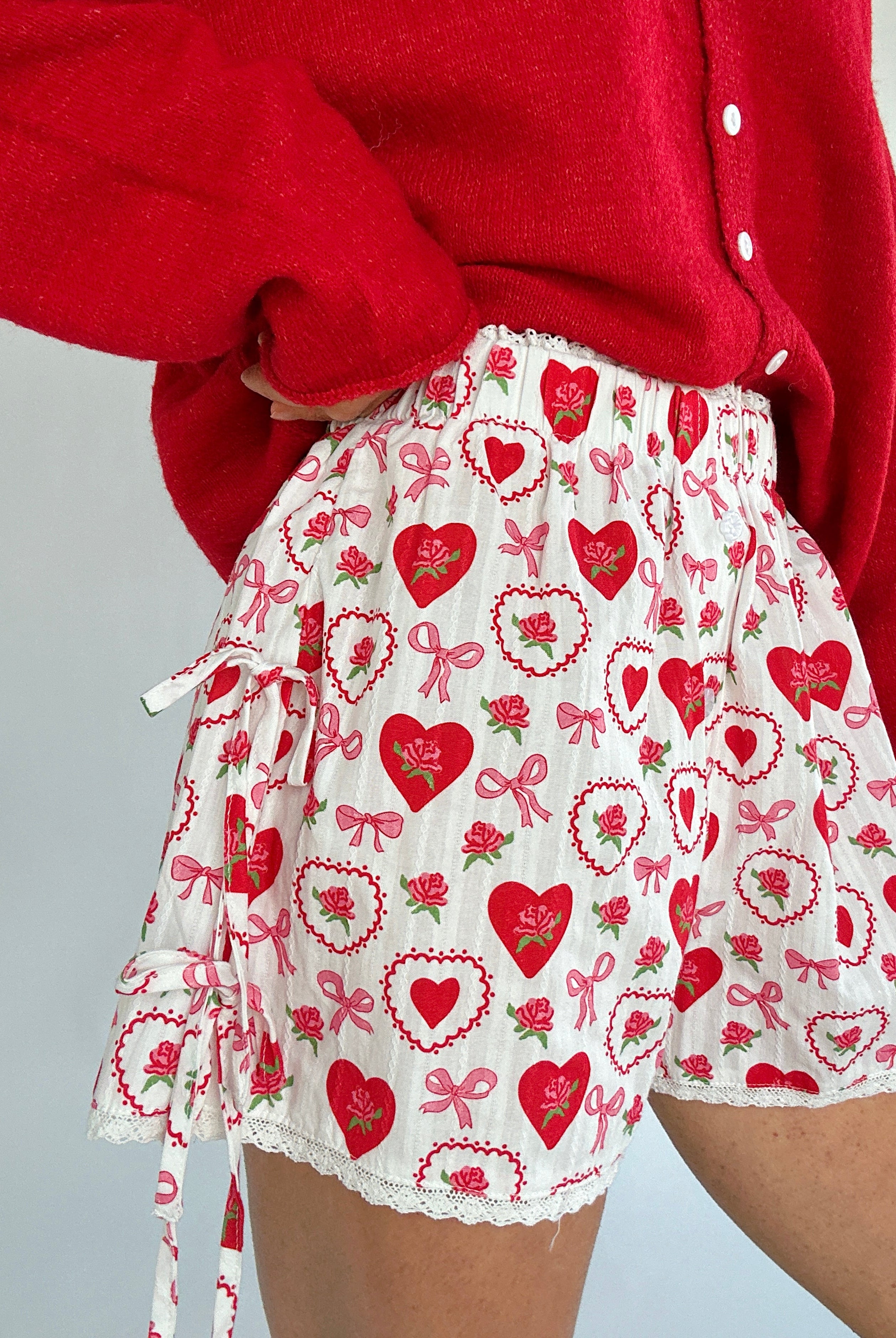 Person wearing a red cardigan and a white shorts with red heart and bow pattern showing side tie details