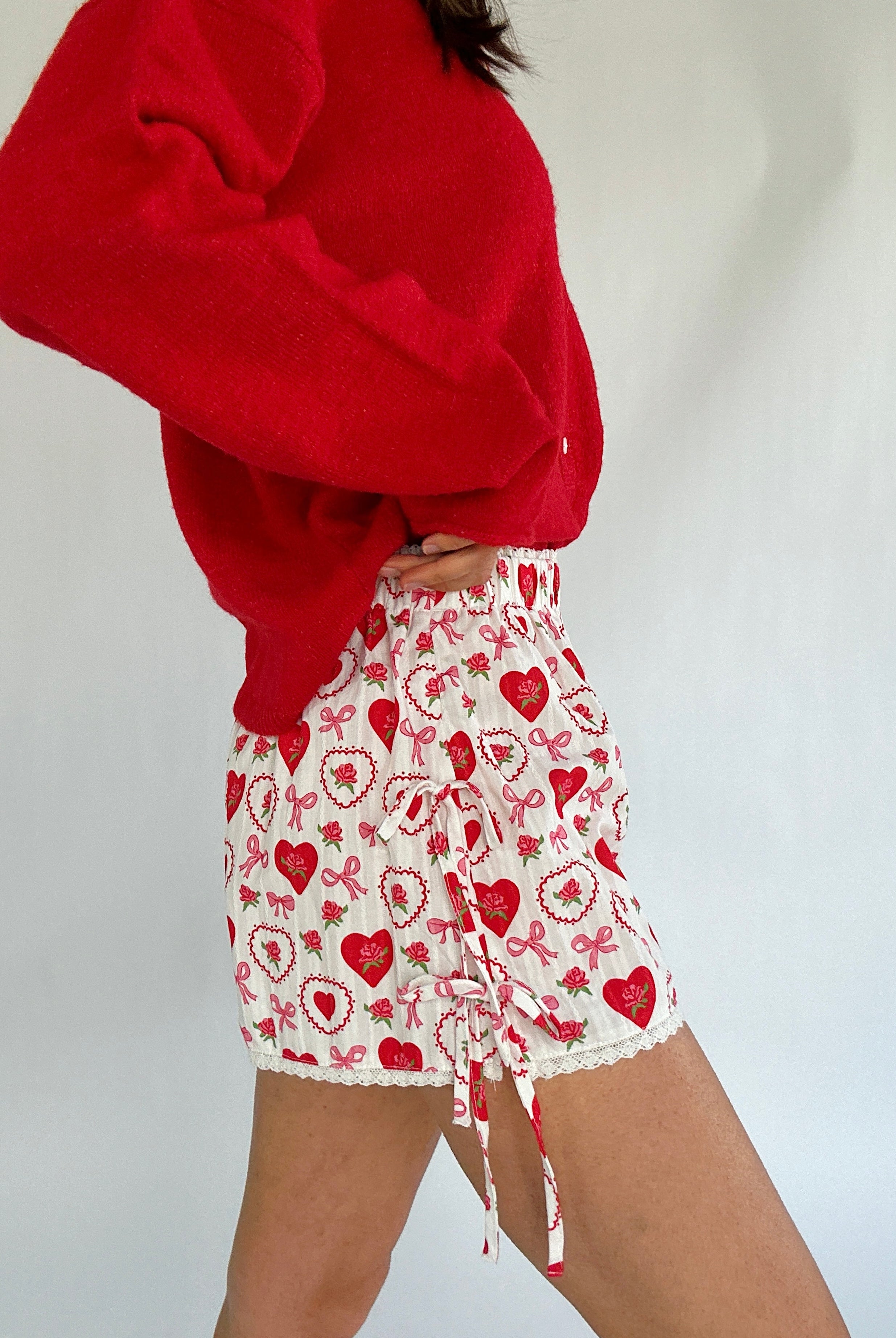 Person wearing a red cardigan and white shorts with red heart patterns on a plain background showing side details