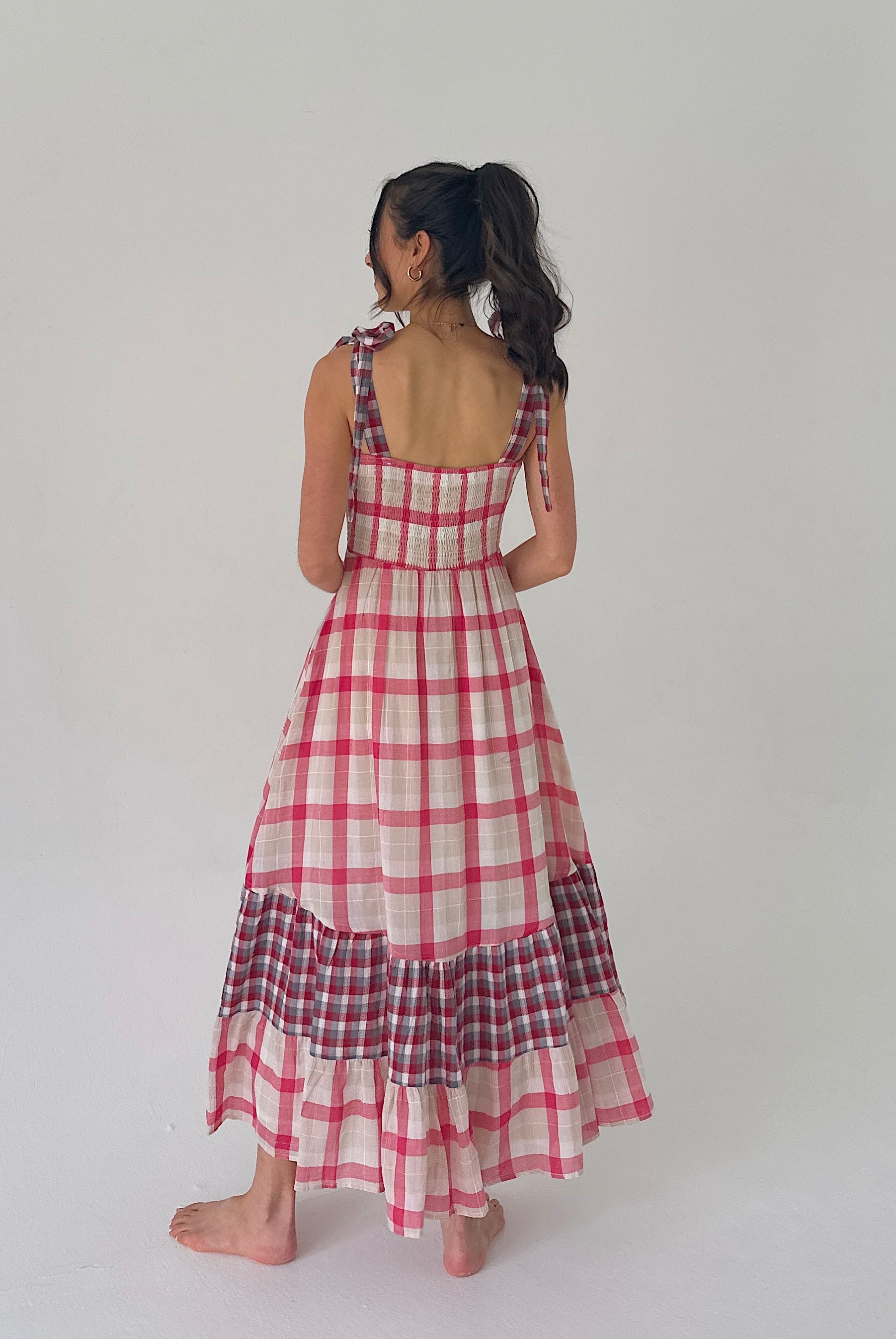 Woman wearing a red and white checkered dress on a plain background showing back