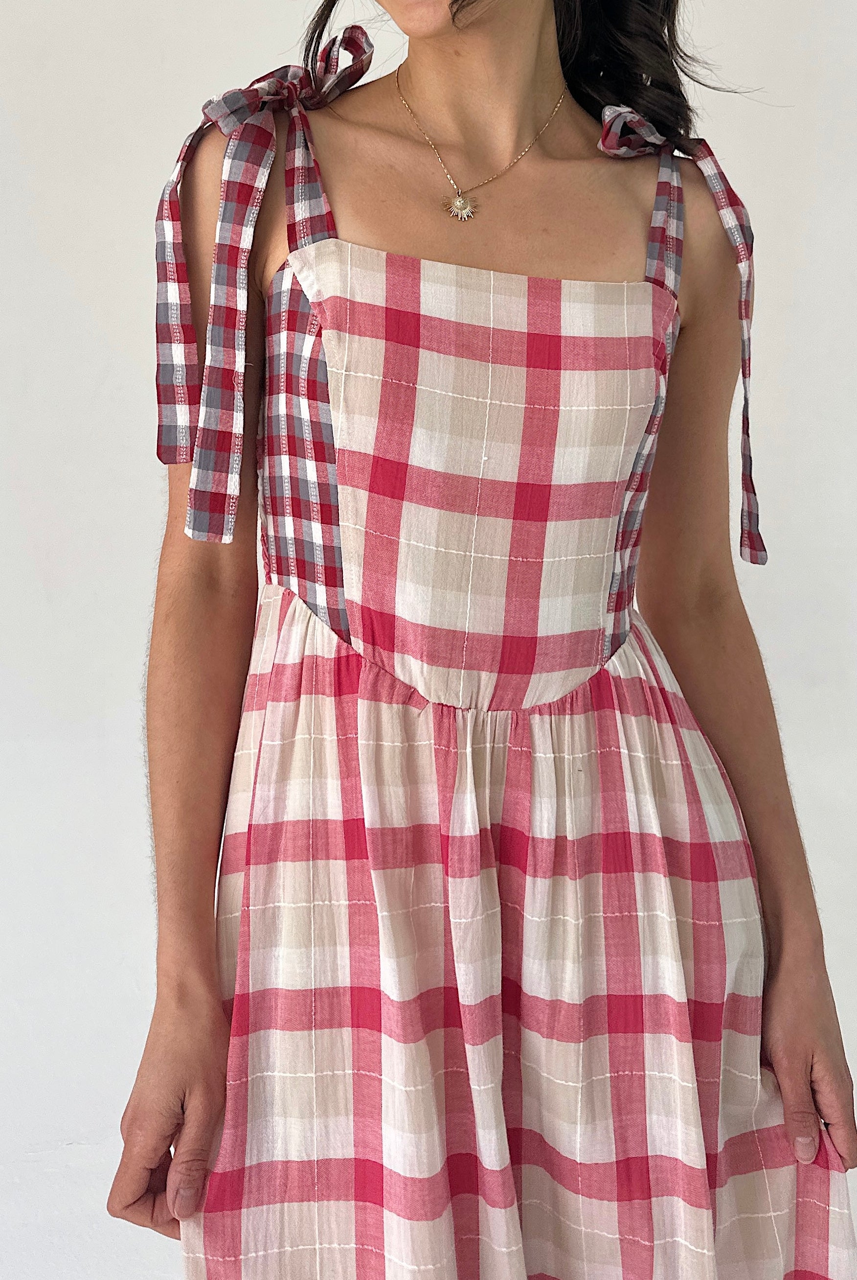 Red and white checkered dress with tied sleeves on a plain background