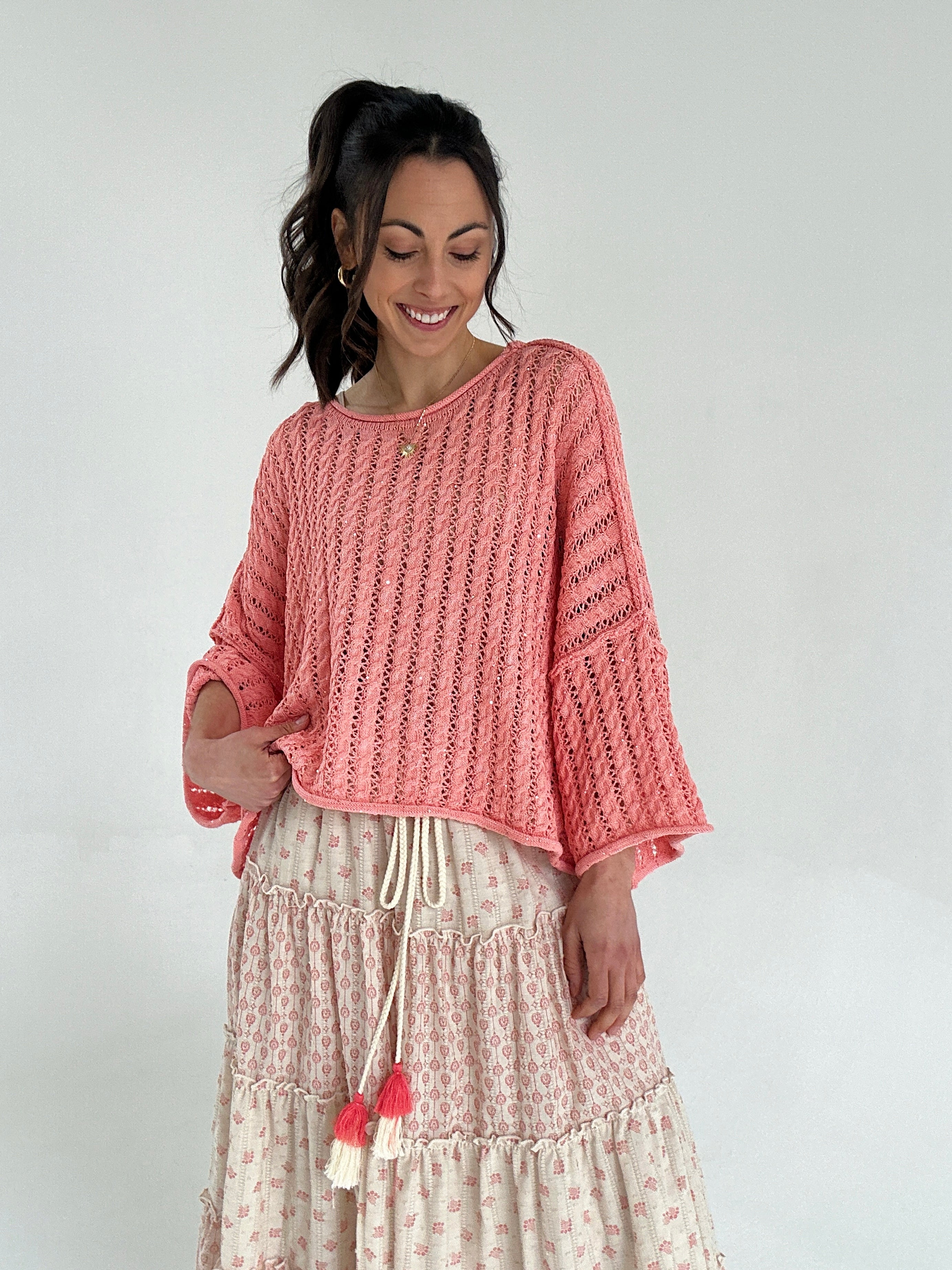 Woman wearing a coral knitted top and patterned skirt on a plain background