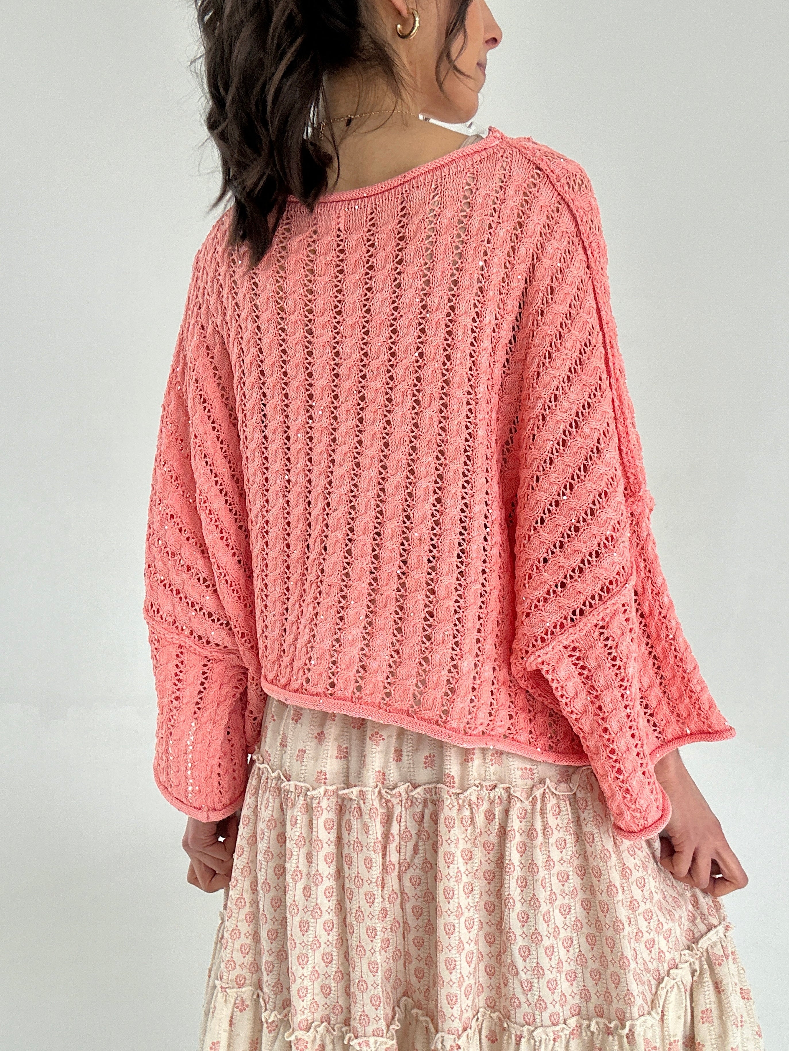 Person wearing a pink knitted sweater with a beige skirt on a plain background showing back