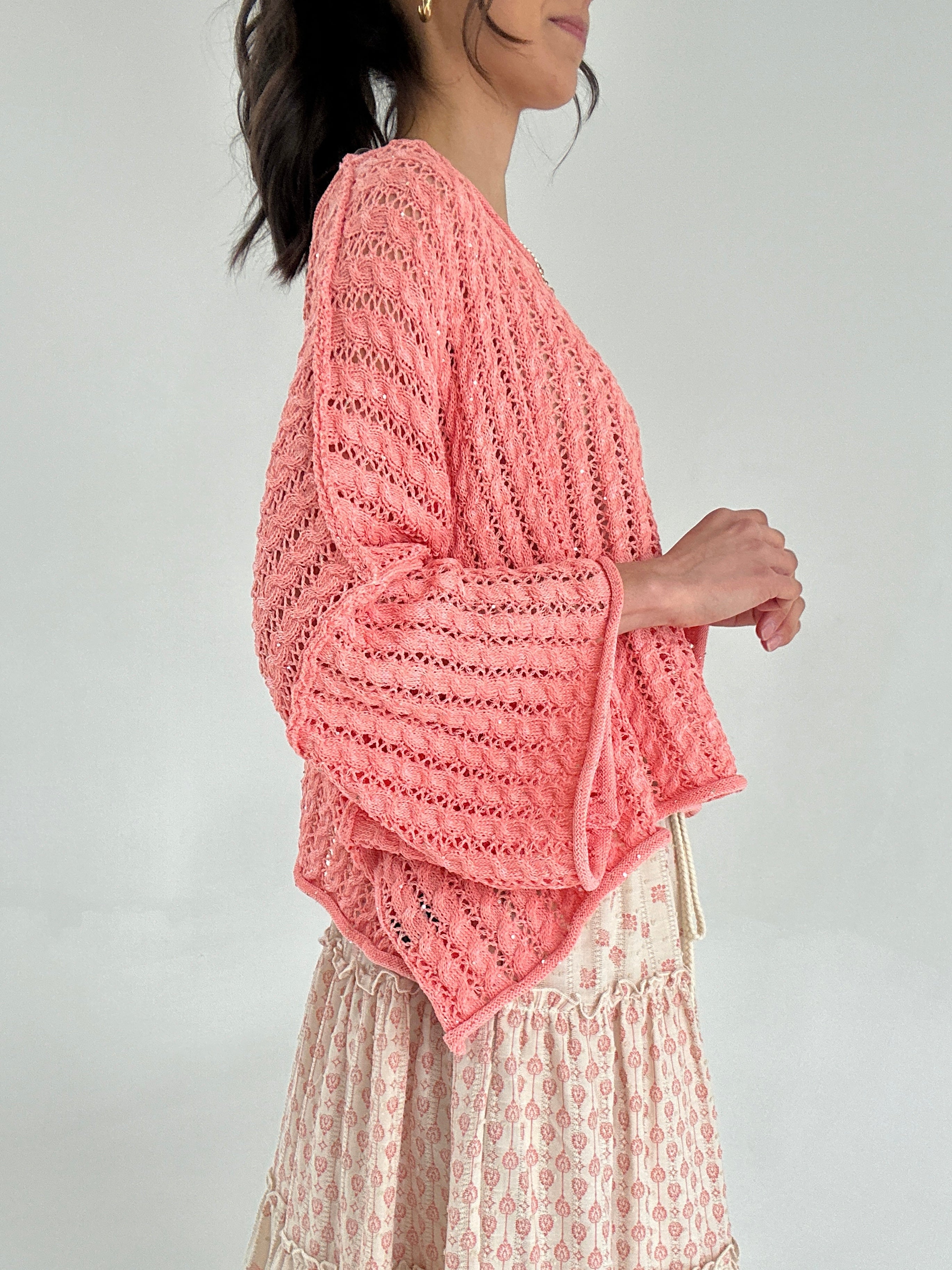 Woman wearing a coral crochet top against a plain background from side