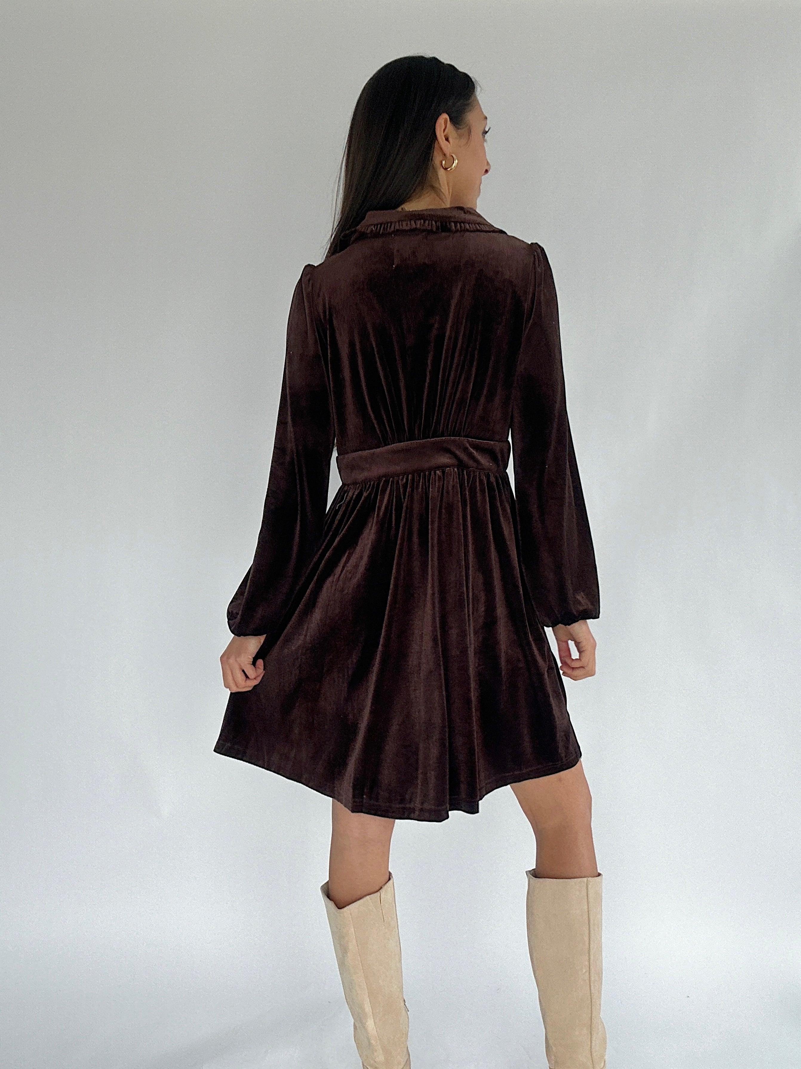Woman wearing a brown velvet mini dress with long sleeves standing against a plain background.