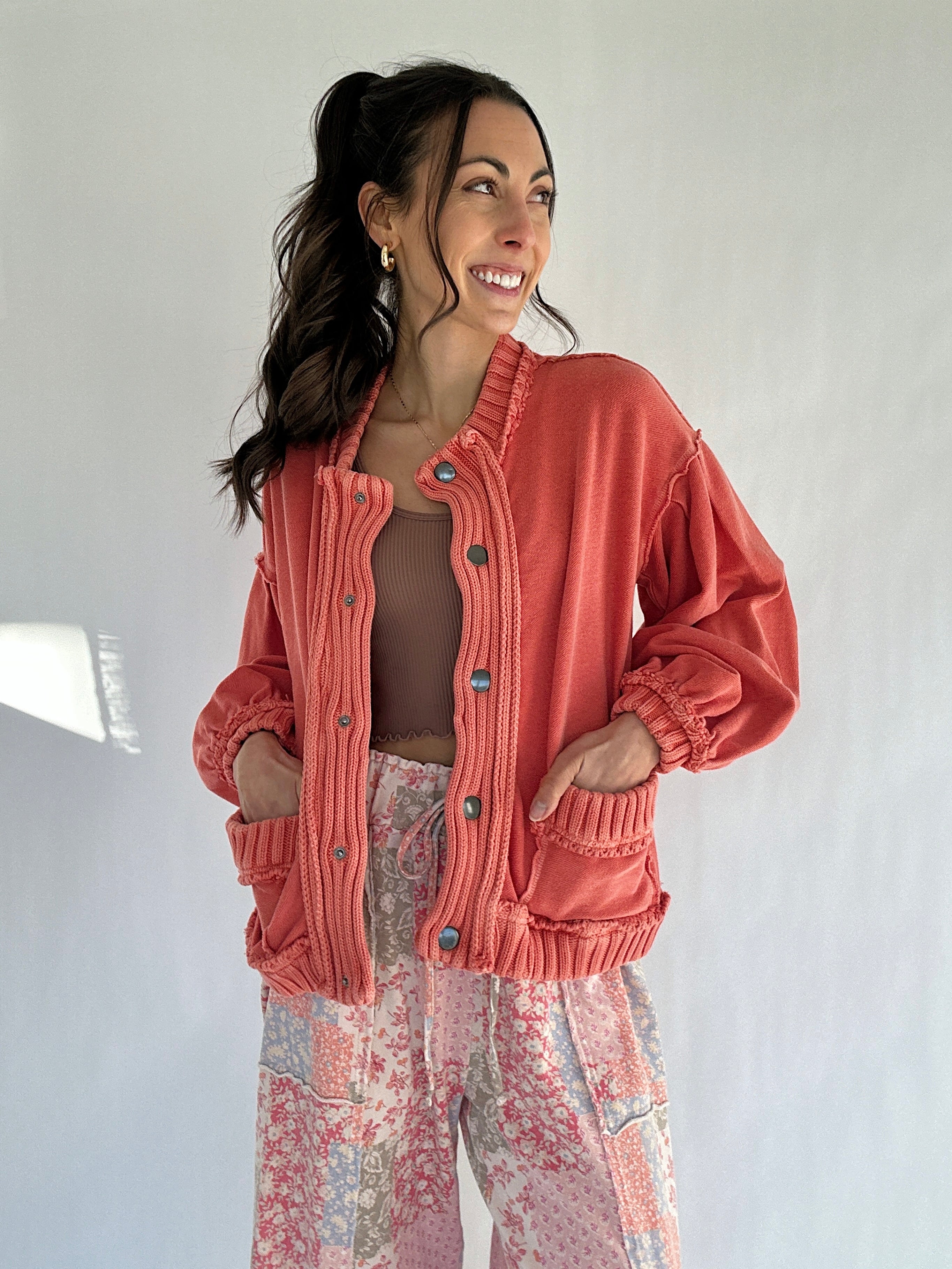 Woman wearing a coral cardigan jacket and patterned pants against a white background