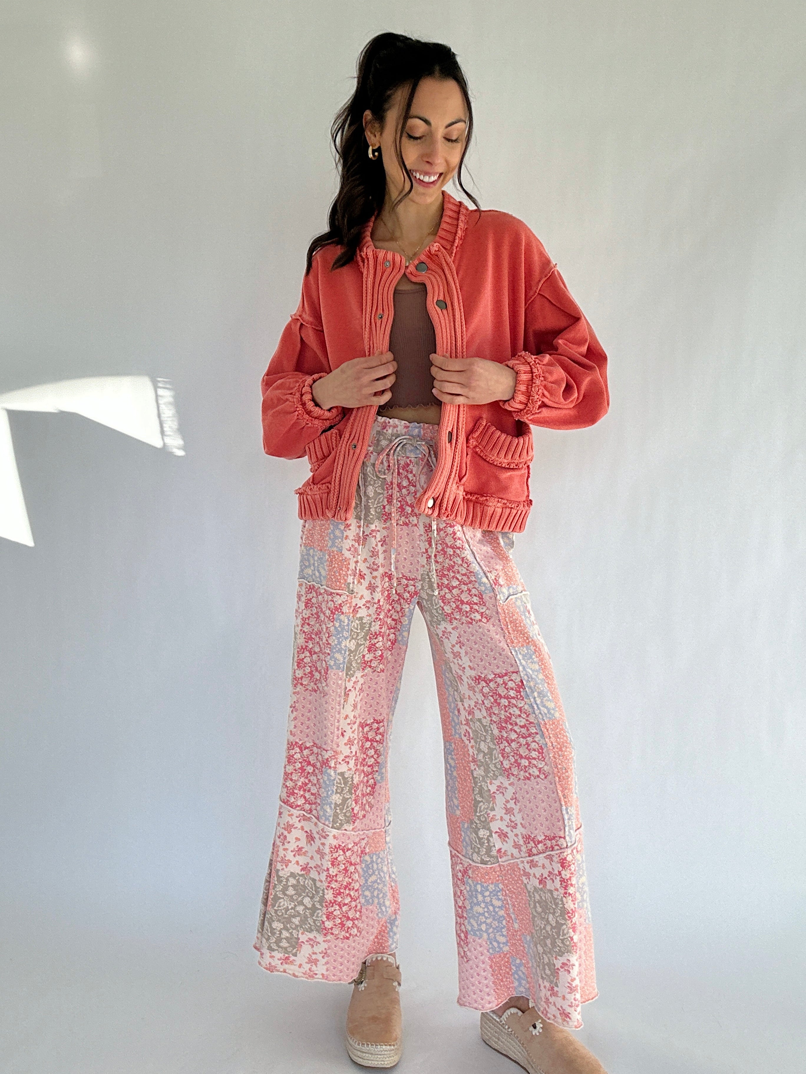 Woman wearing a coral jacket and floral pants against a white background