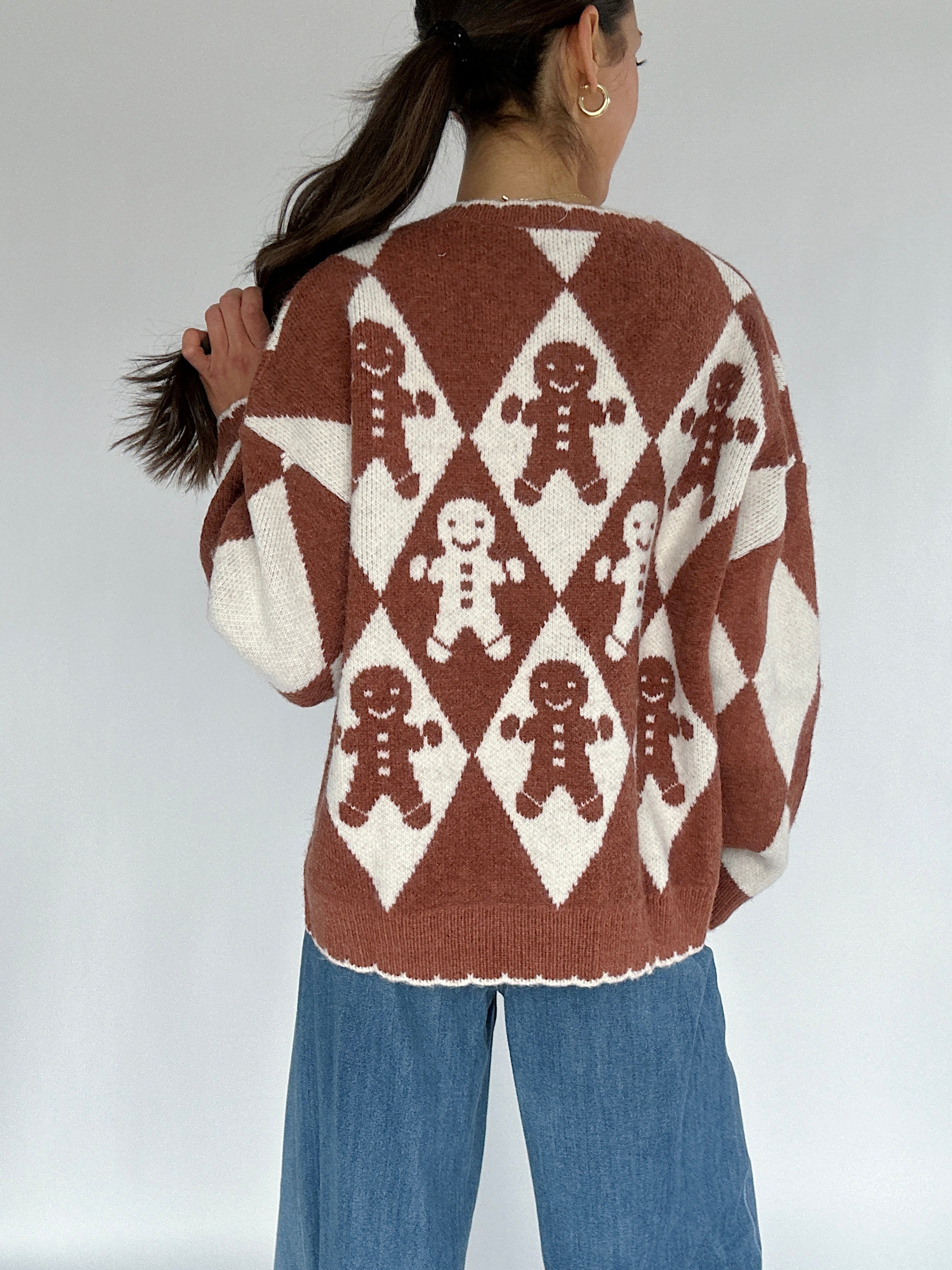 Person wearing a brown sweater with gingerbread man pattern on a plain background showing back