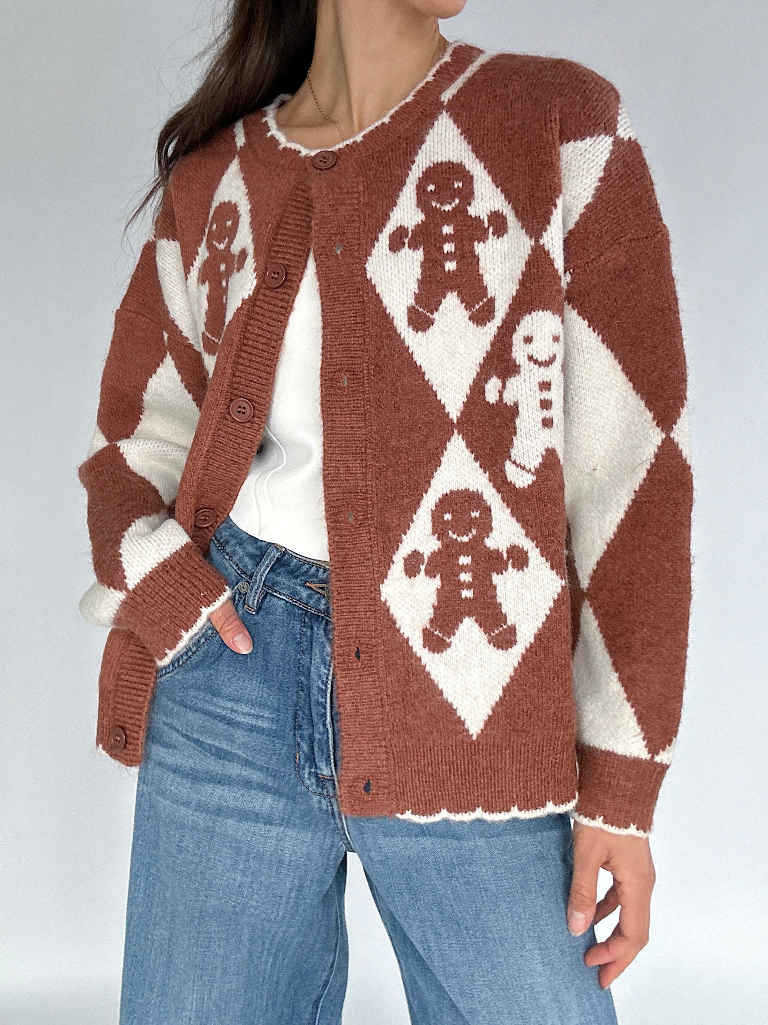 Person wearing a brown and white patterned cardigan with gingerbread men design on a plain background