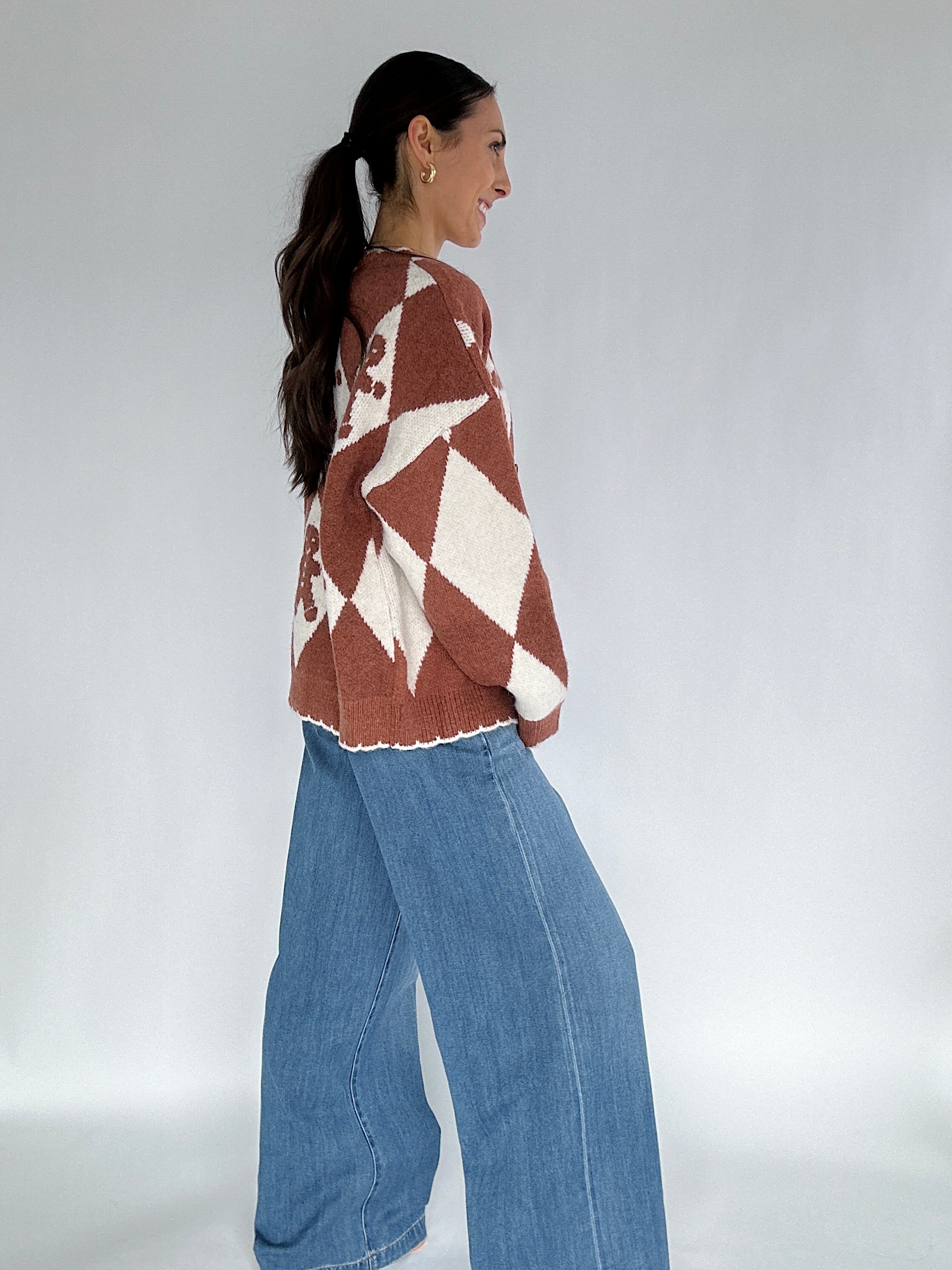 Woman wearing a patterned sweater and blue jeans against a plain background side view