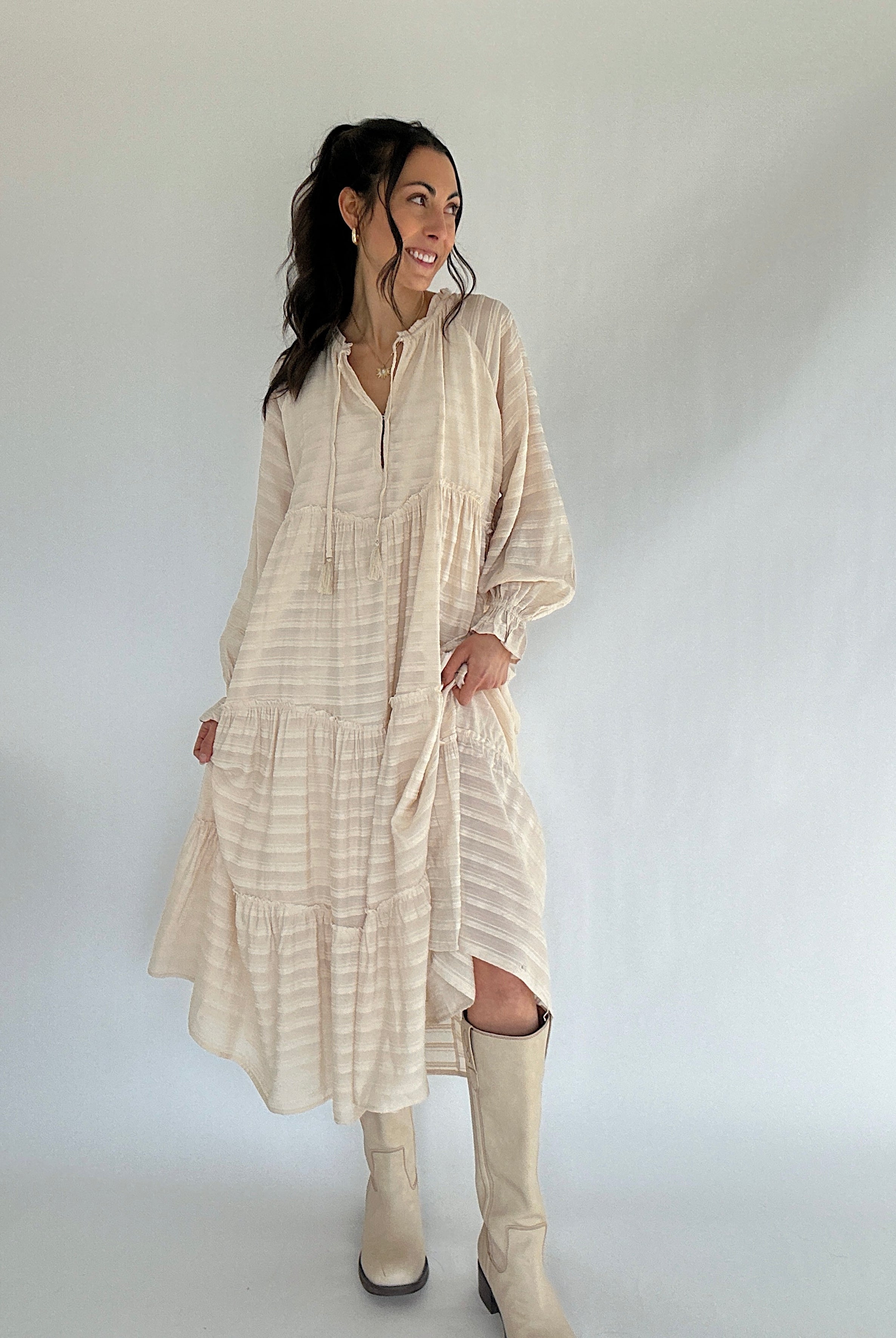 Woman wearing a beige dress and boots against a white background