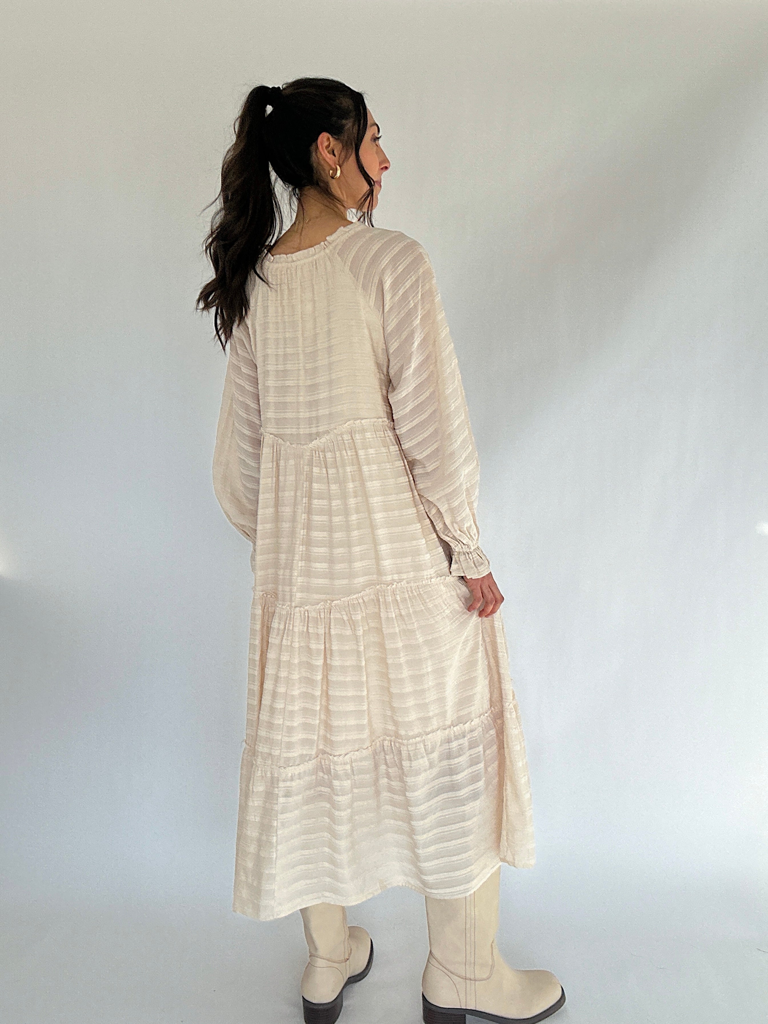 Woman wearing a beige long-sleeve dress against a white background from the back