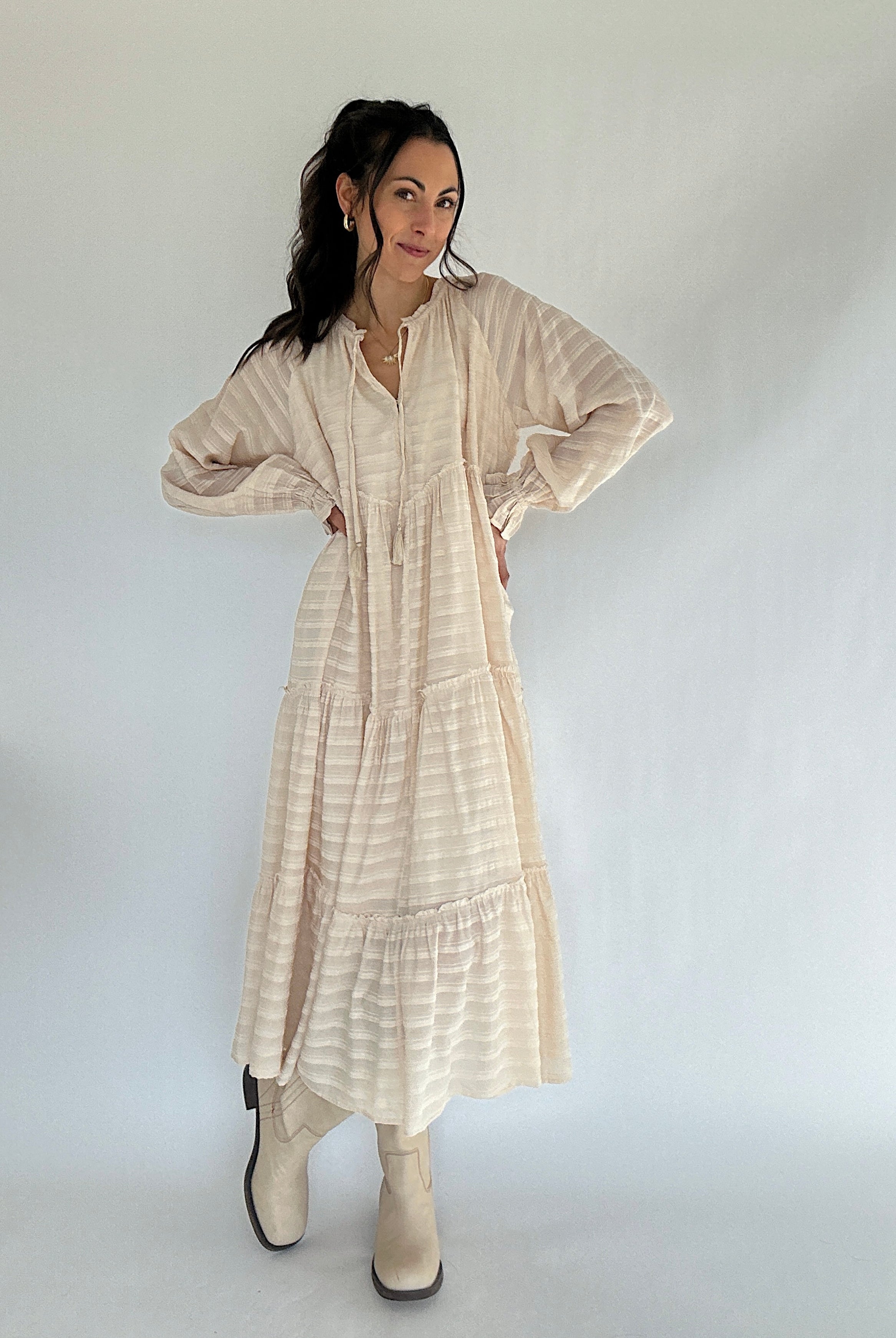 Woman wearing a beige dress with long sleeves against a white background