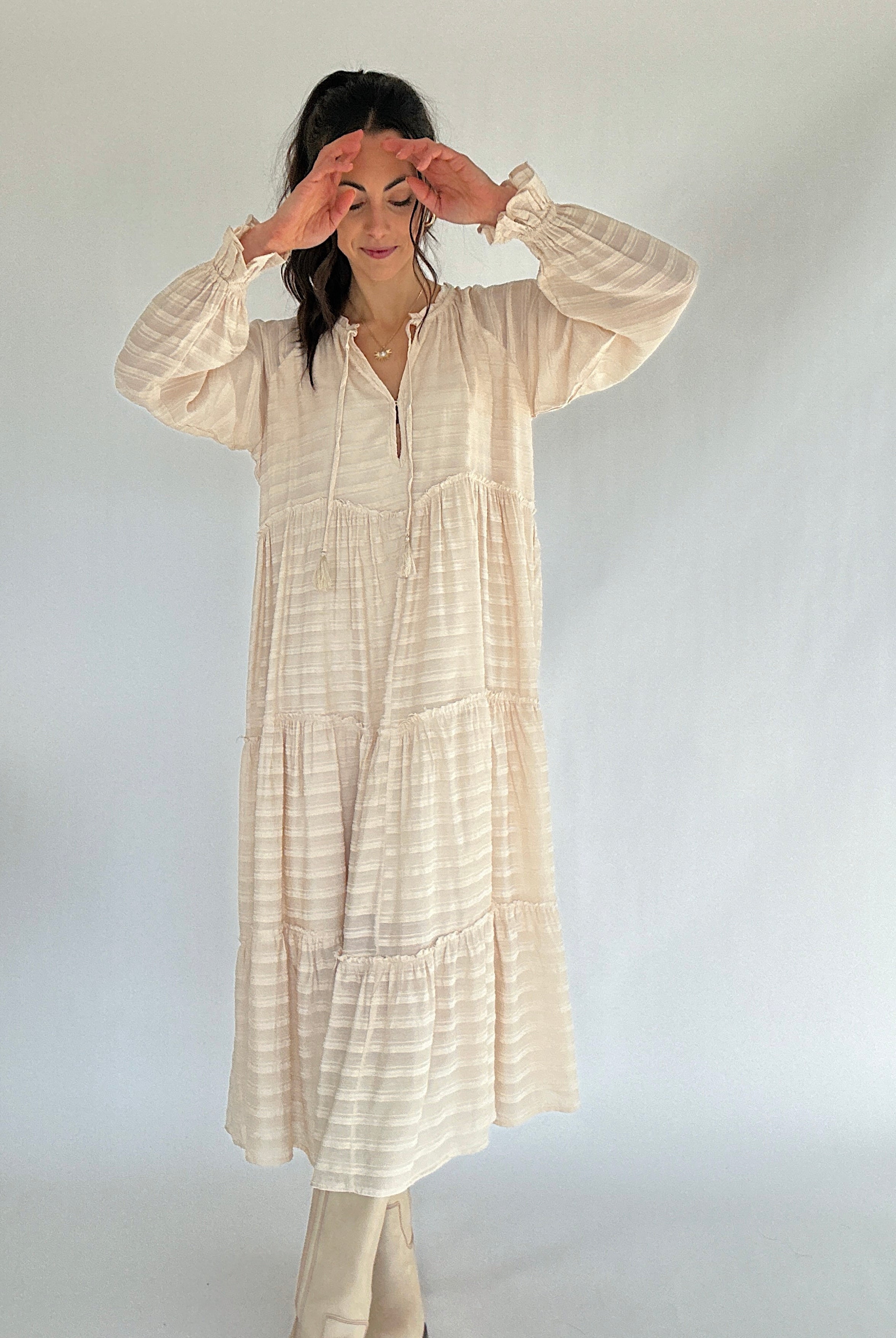 Woman wearing a long, beige-colored dress against a plain background