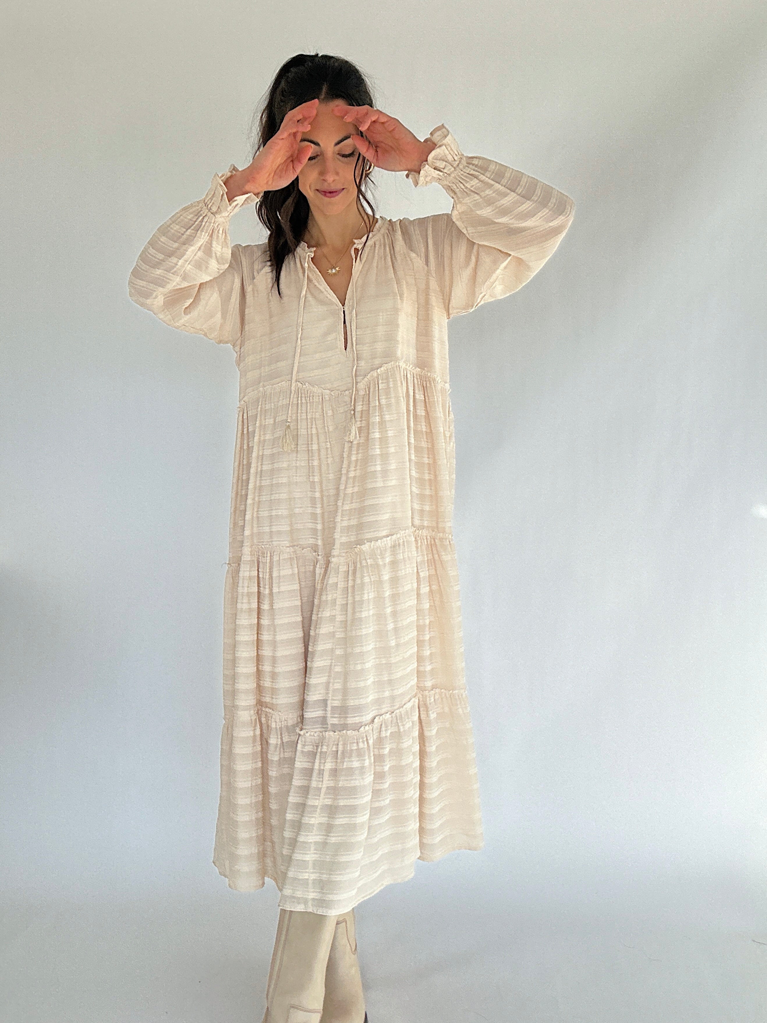 Woman wearing a long, beige-colored dress against a plain background