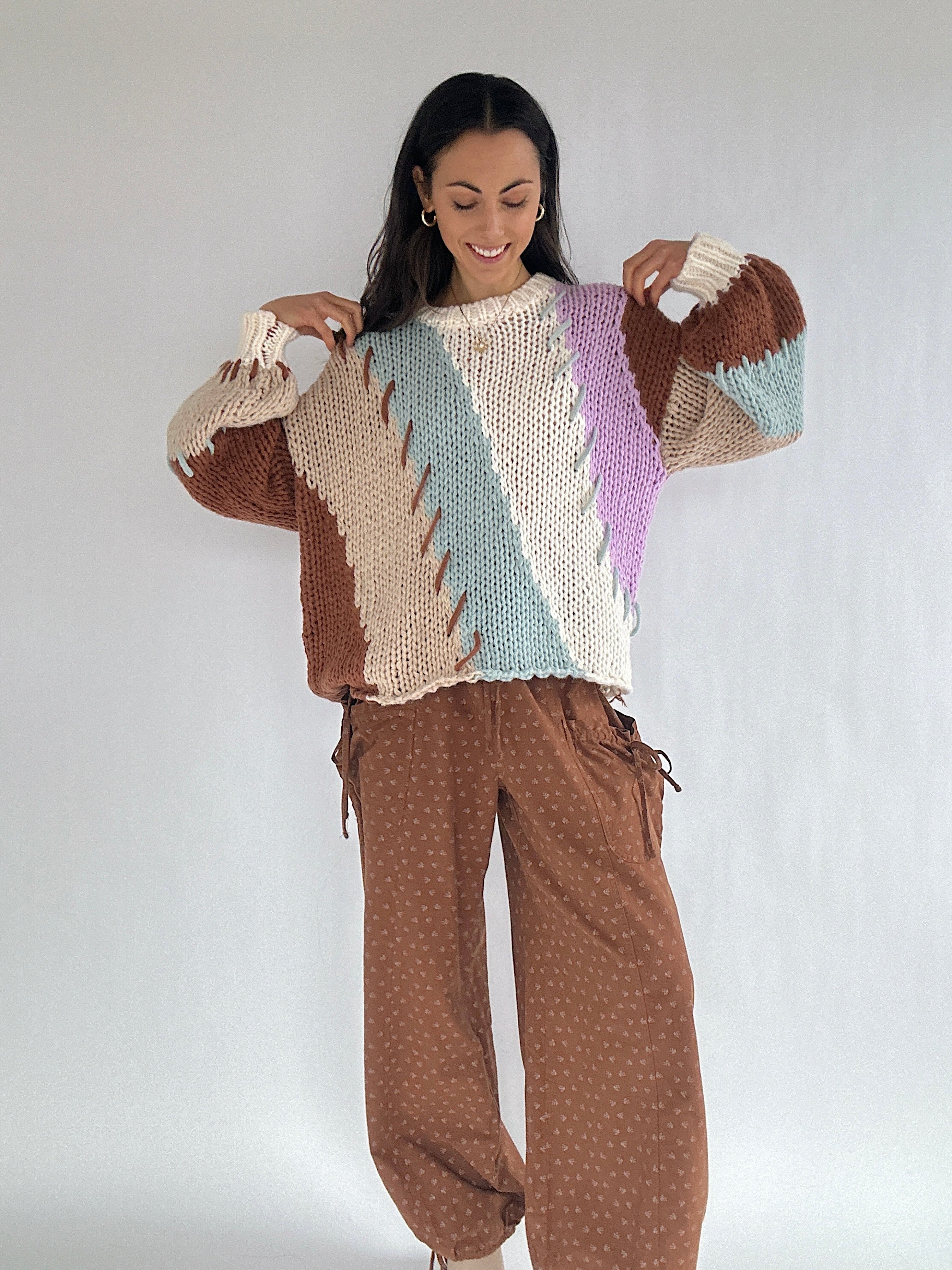 Woman wearing a colorful knitted sweater and brown pants against a white background