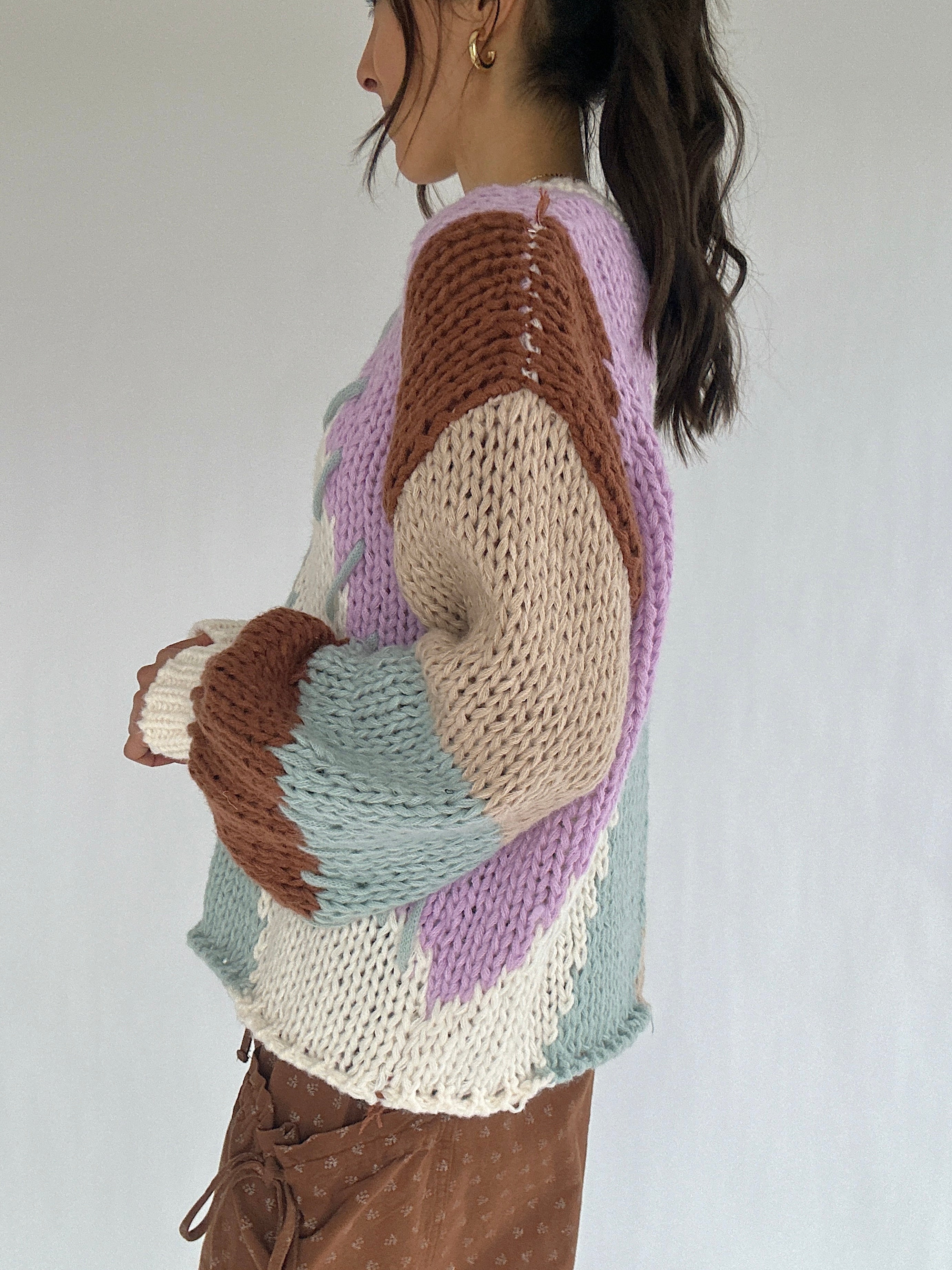 Person wearing a multicolored knit sweater against a plain background from the side