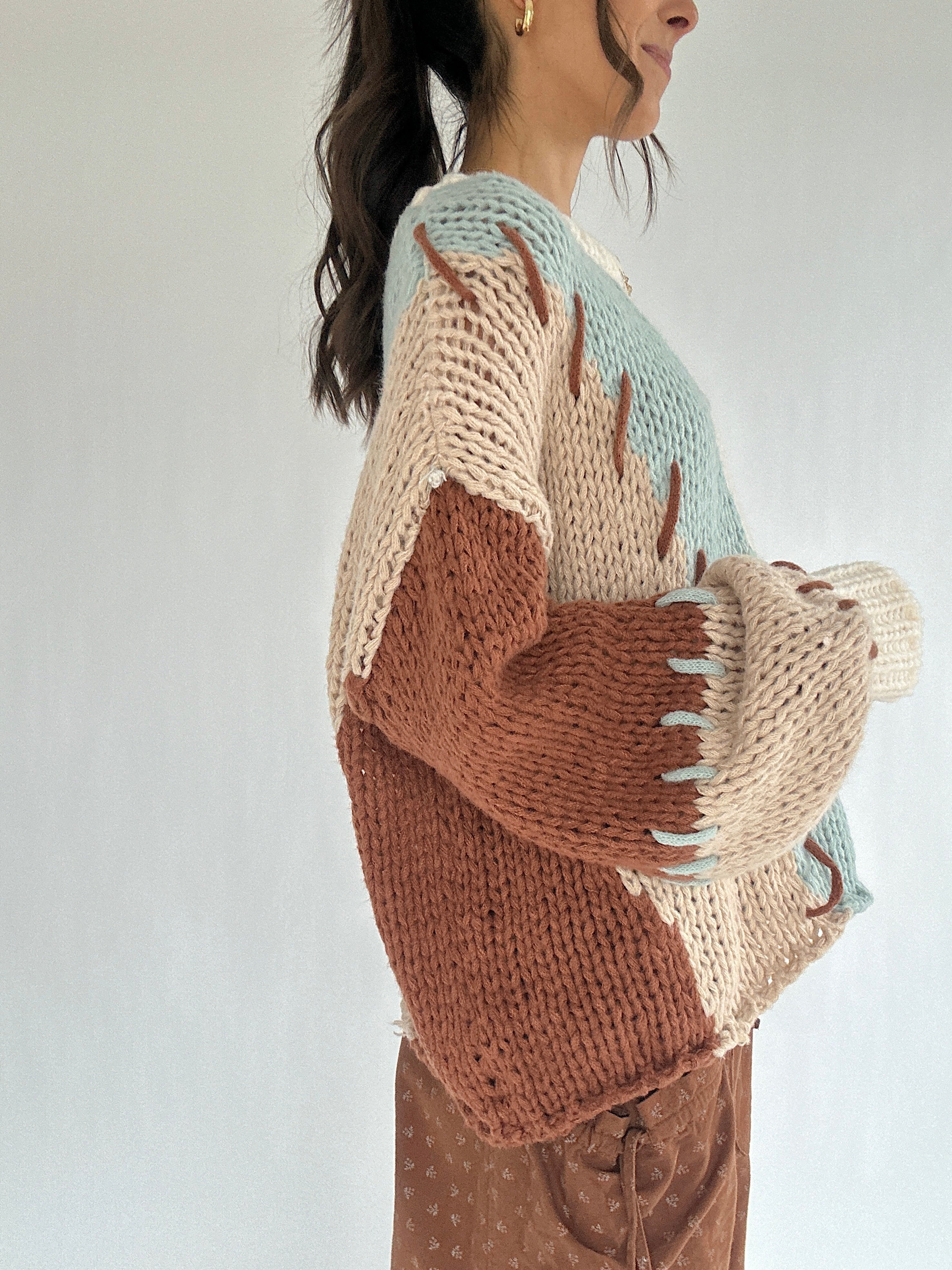 Person wearing a chunky knit sweater with stitch accents on a plain background from the side