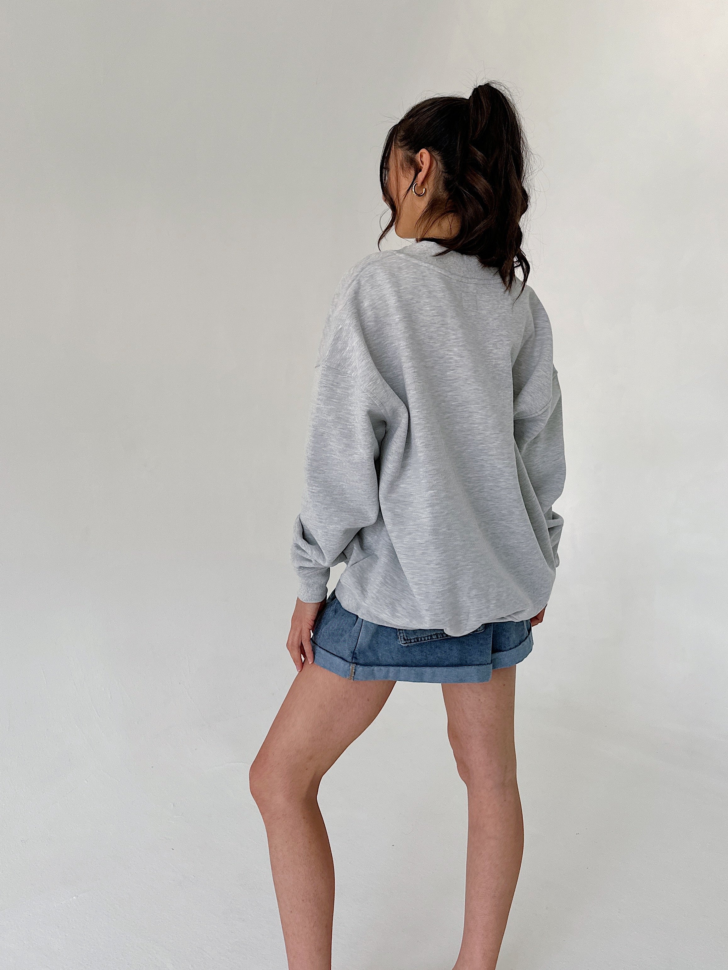 Person wearing a gray sweatshirt and denim shorts against a plain background