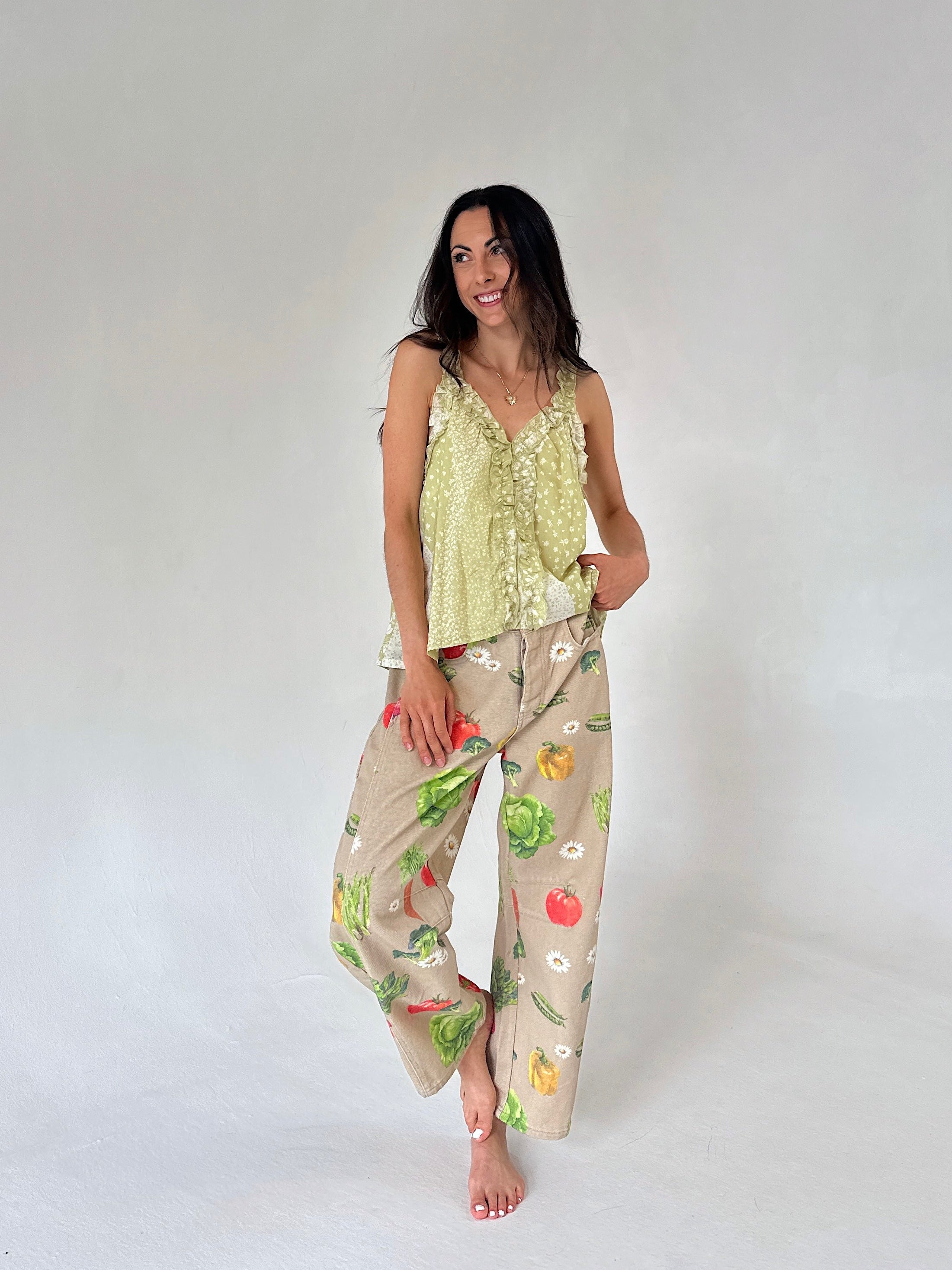 A woman modeling a light yellow-green ruffled camisole top and barrel pants with a colorful vegetable print, set against a plain light gray studio background.