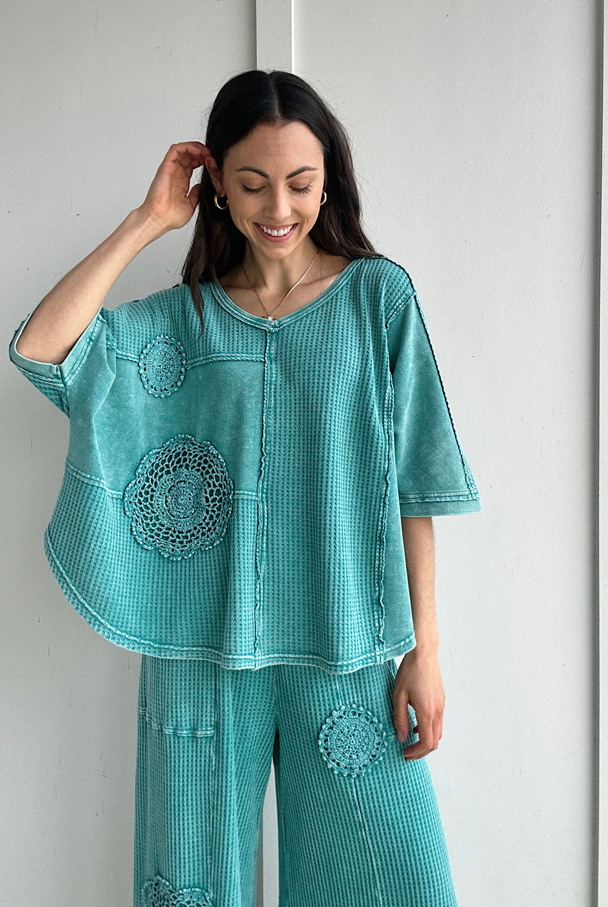 Woman wearing a teal textured outfit with floral crochet patterns against a white background