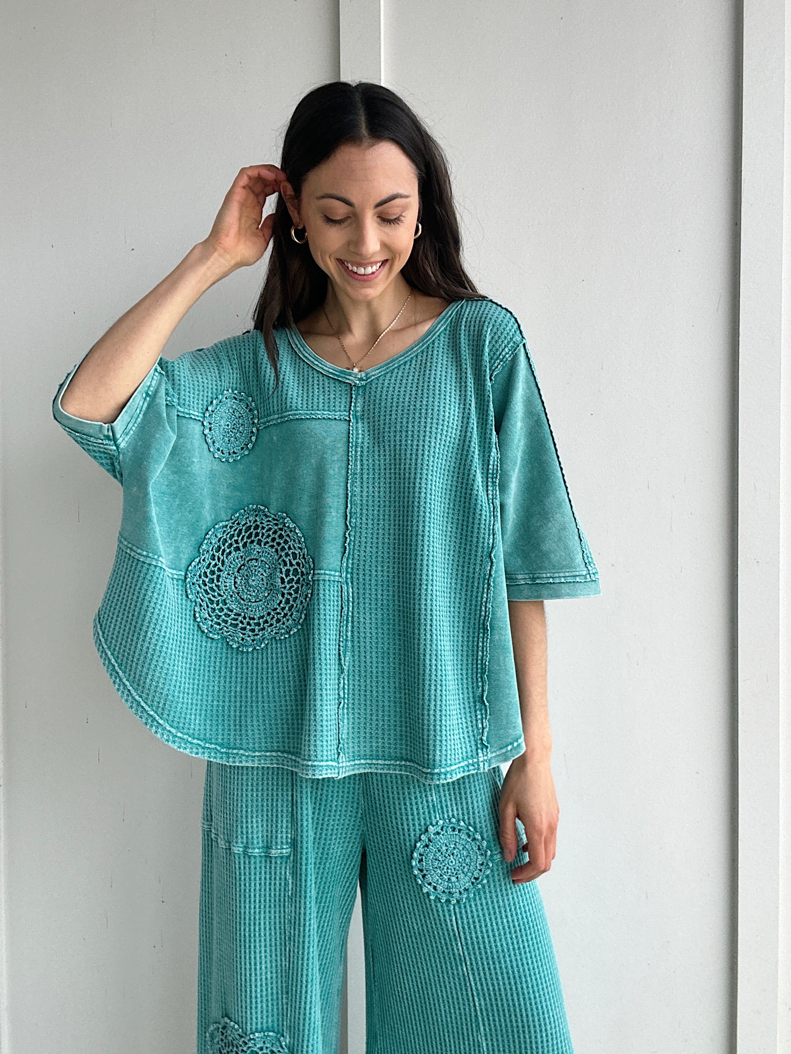 Woman wearing a teal textured outfit with floral crochet patterns against a white background