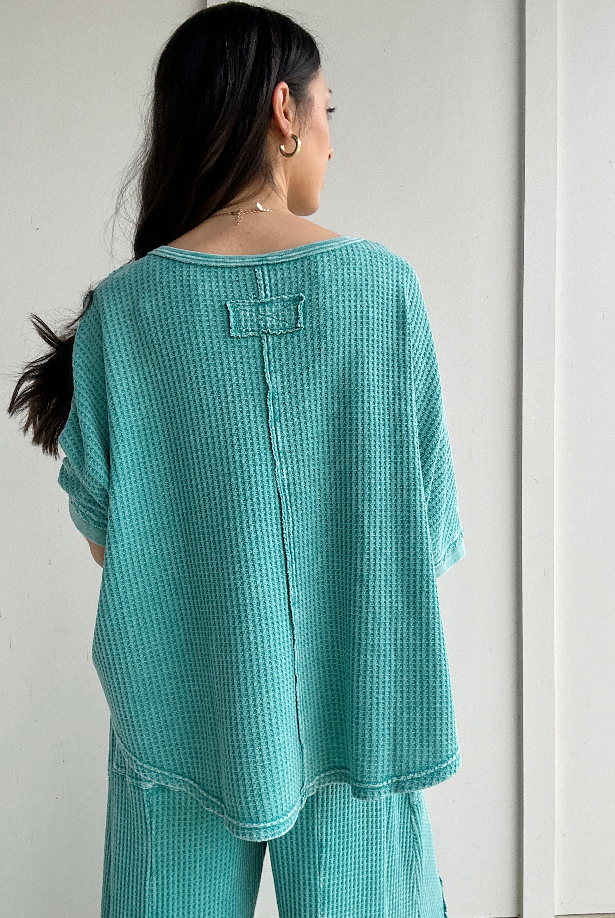 Person wearing a teal textured outfit against a white background showing back