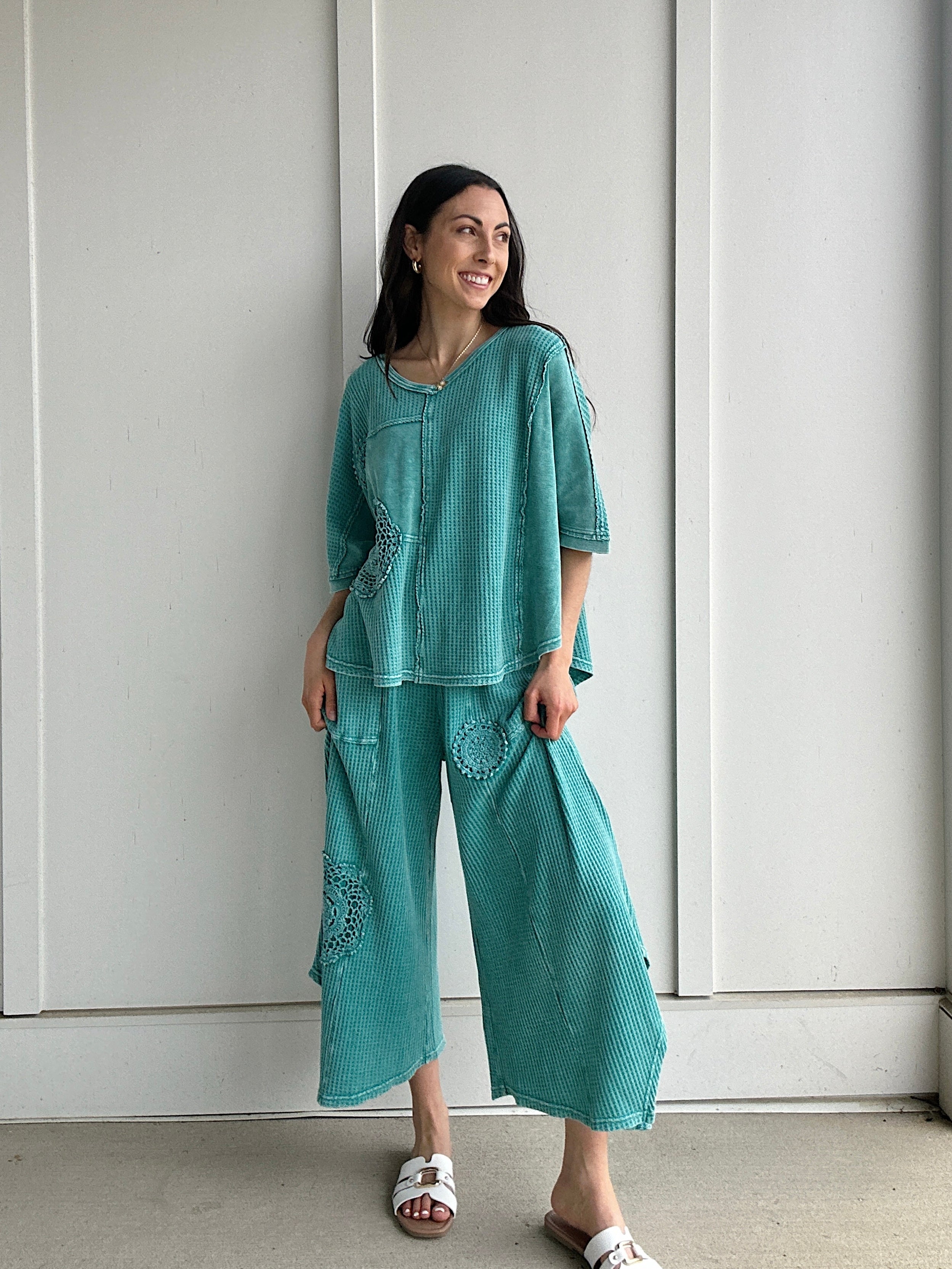 Woman wearing a teal outfit standing against a white wall.