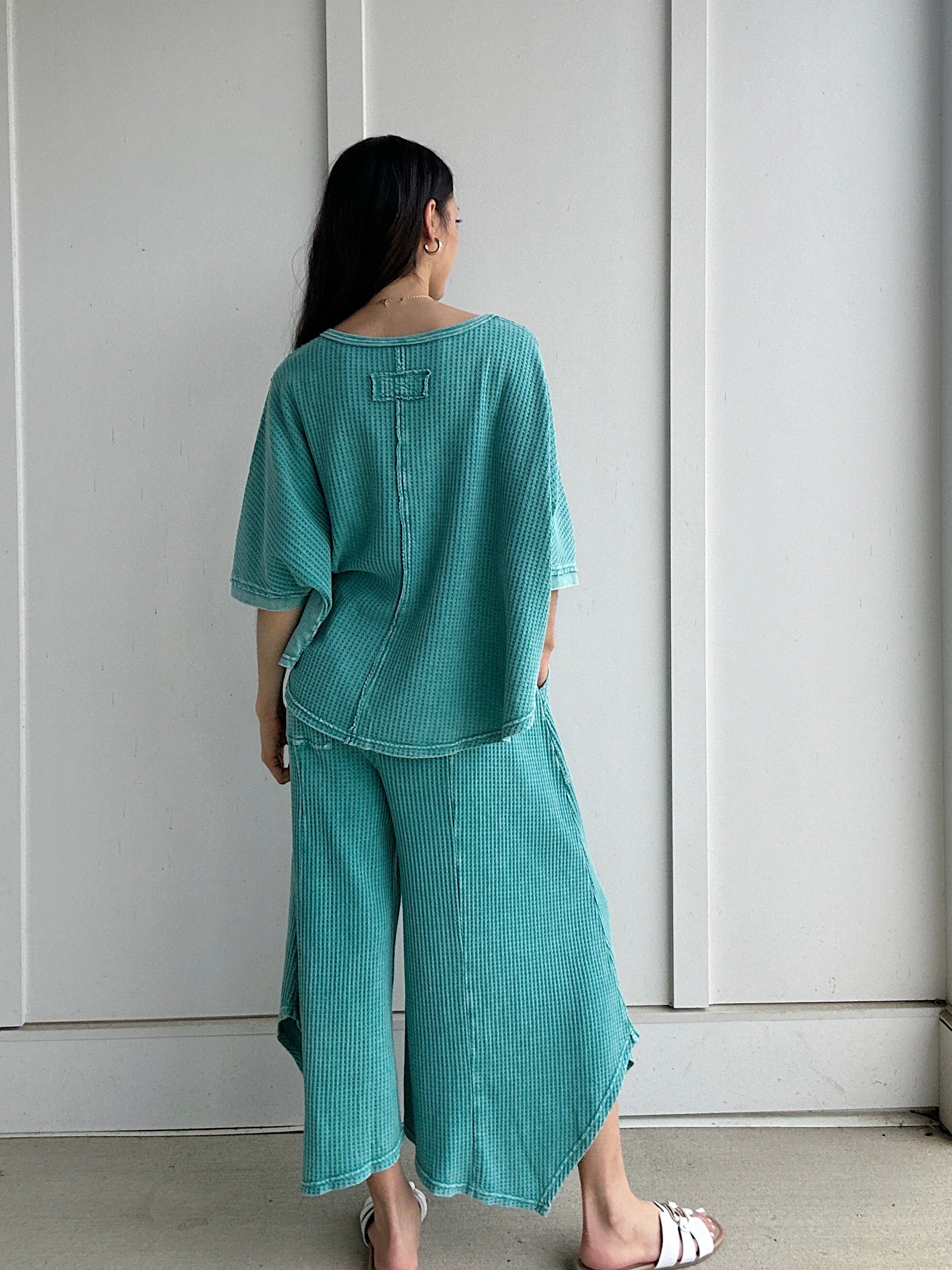 Person wearing a teal outfit standing against a white wall showing back