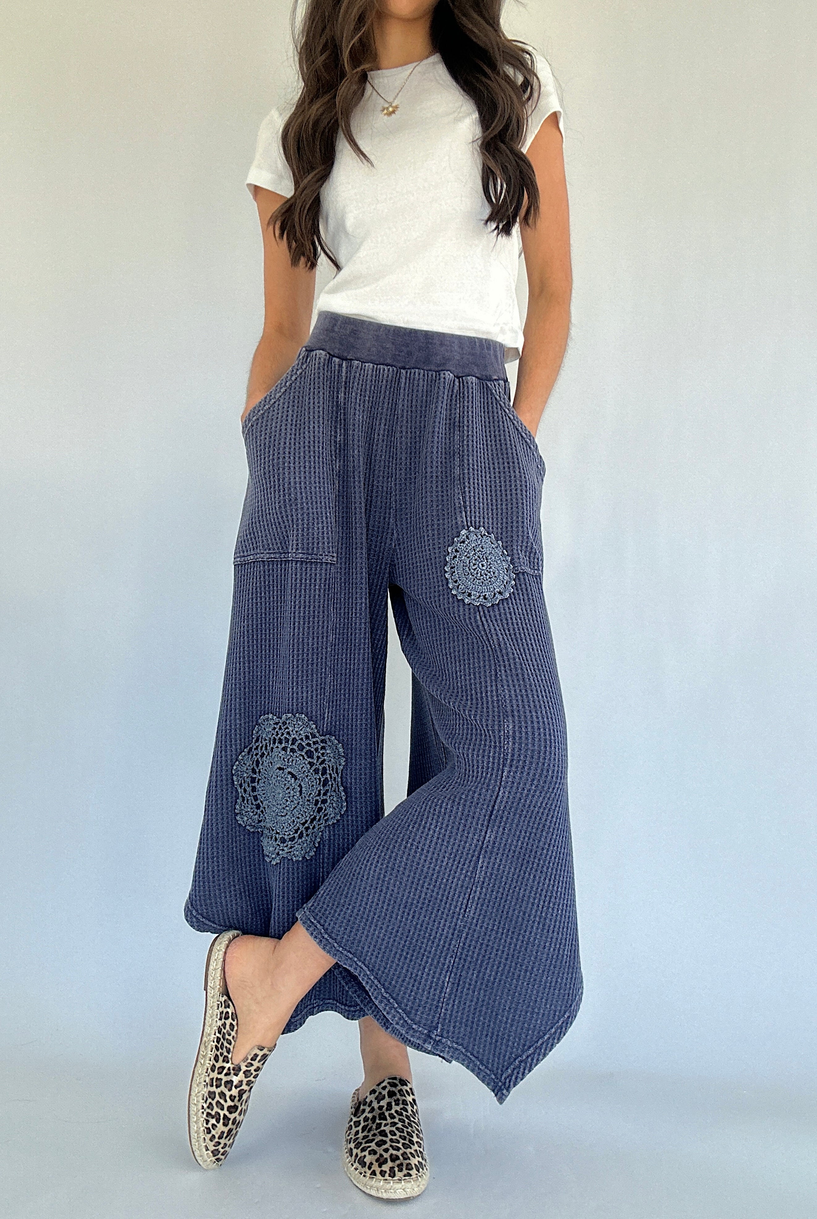 Woman wearing blue waffle knit wide-leg pants with floral crochet embroidery on a white background