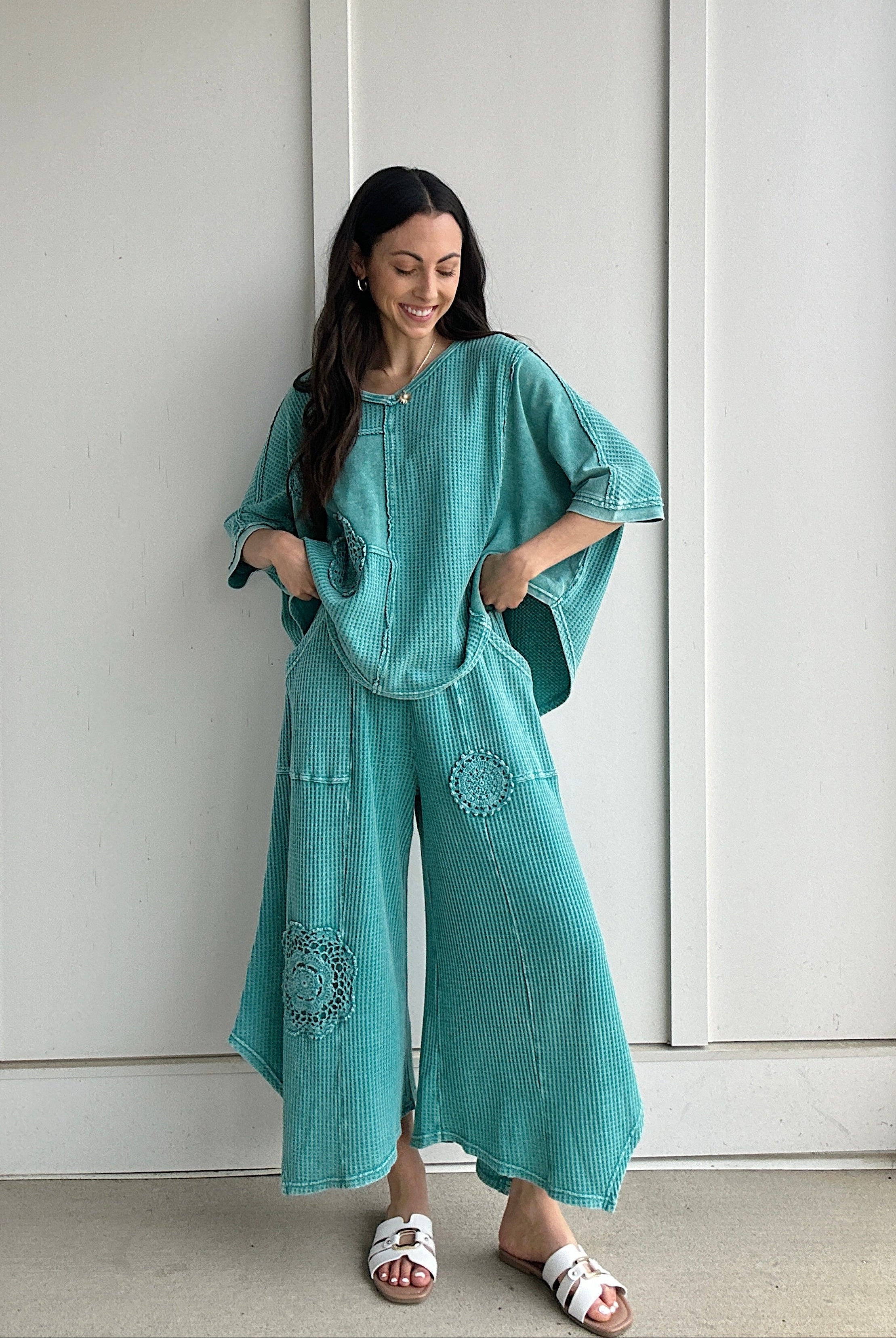 Woman wearing a teal outfit with a matching top and wide-leg pants against a white wall.