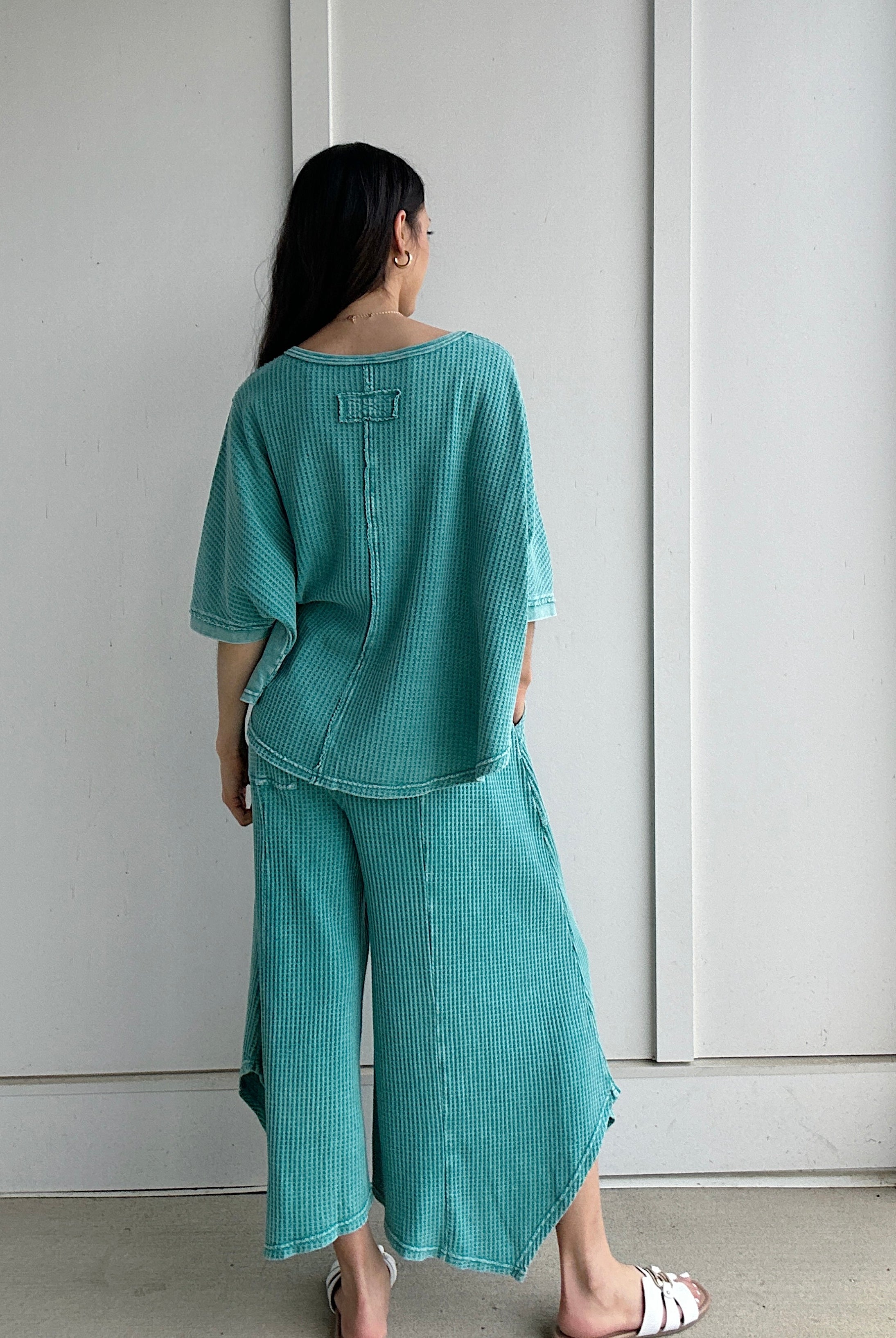 Person wearing a teal outfit standing against a white wall showing back