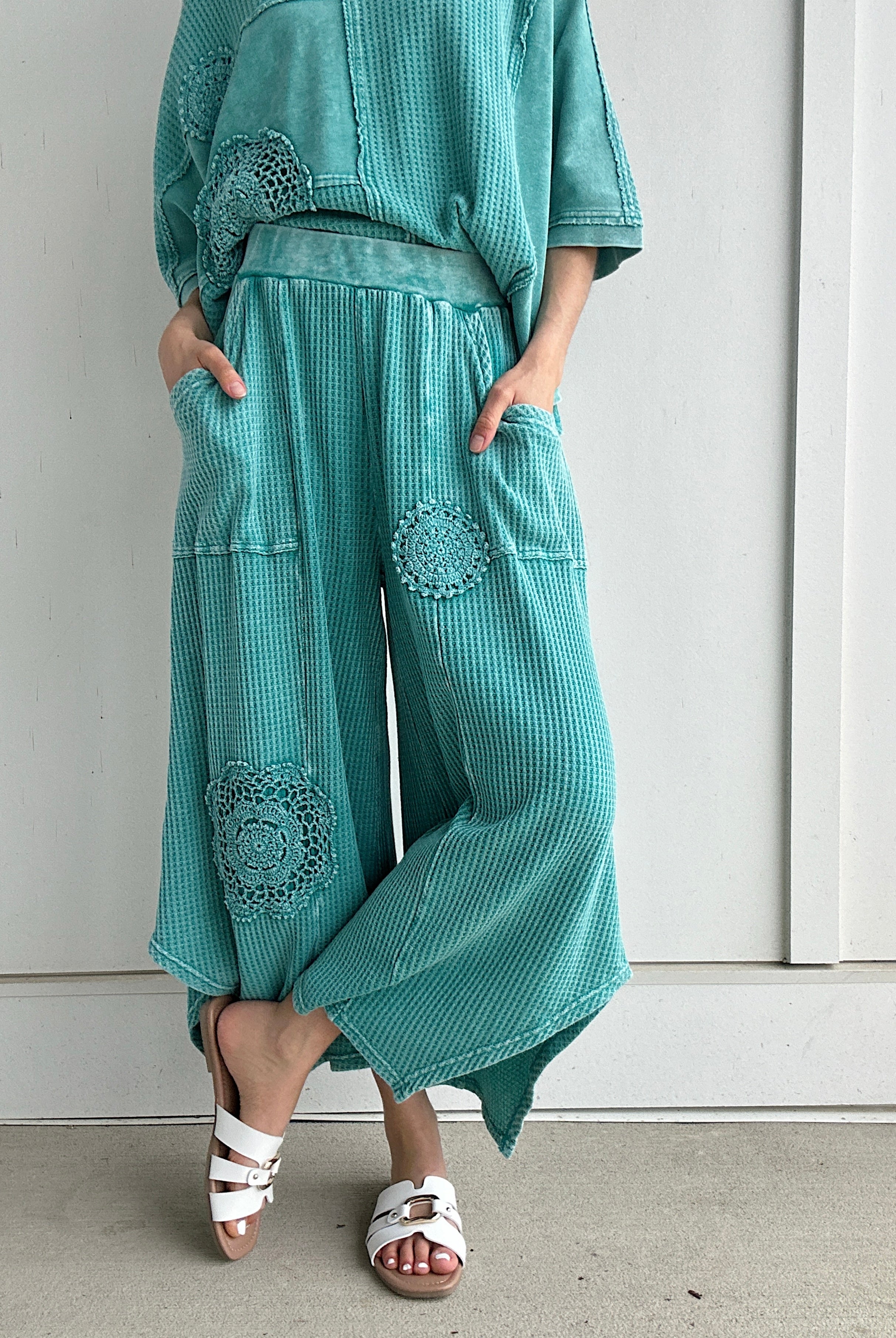 Person wearing teal textured outfit with decorative elements against a white wall.