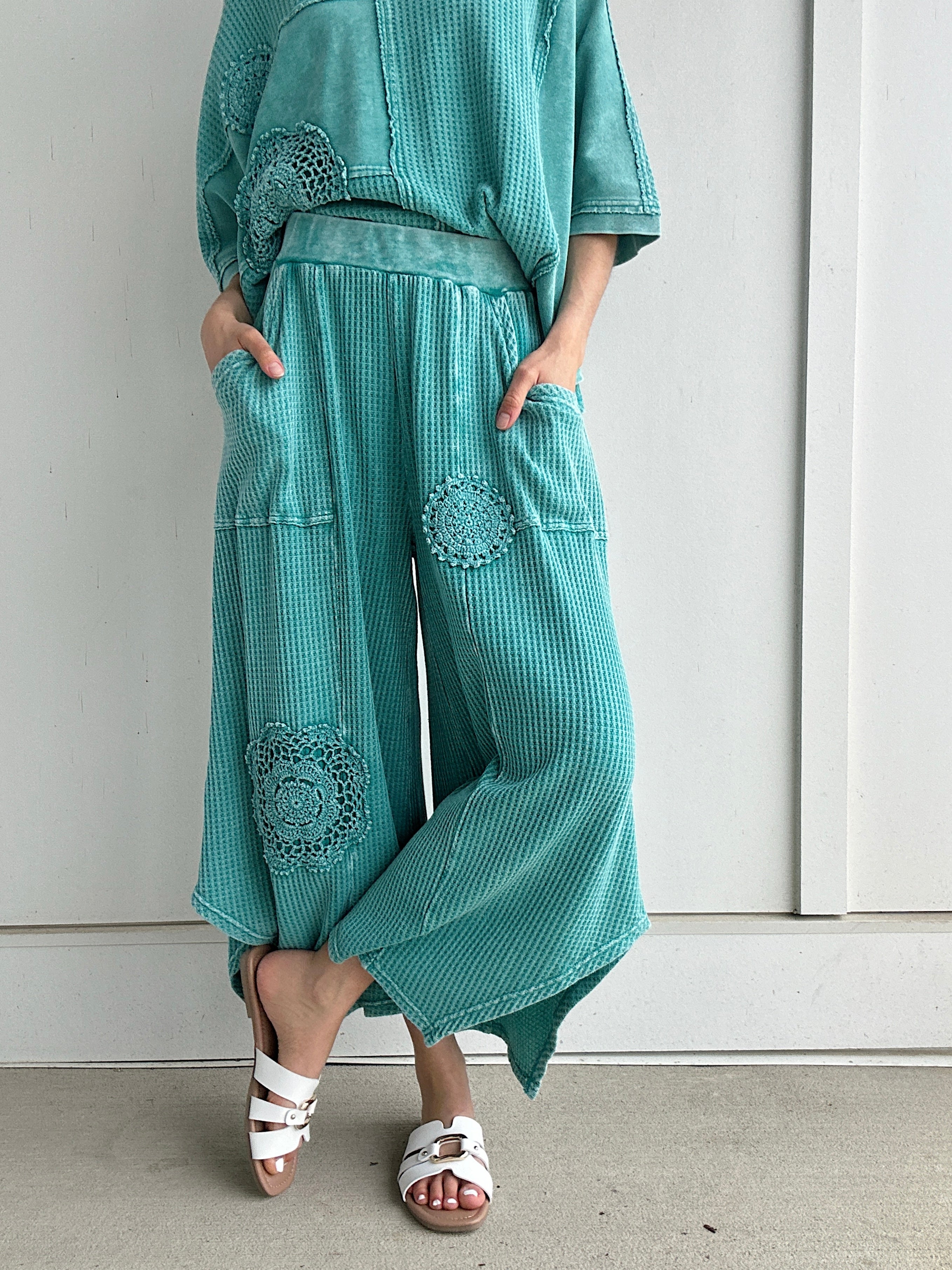 Person wearing teal textured outfit with decorative elements against a white wall.
