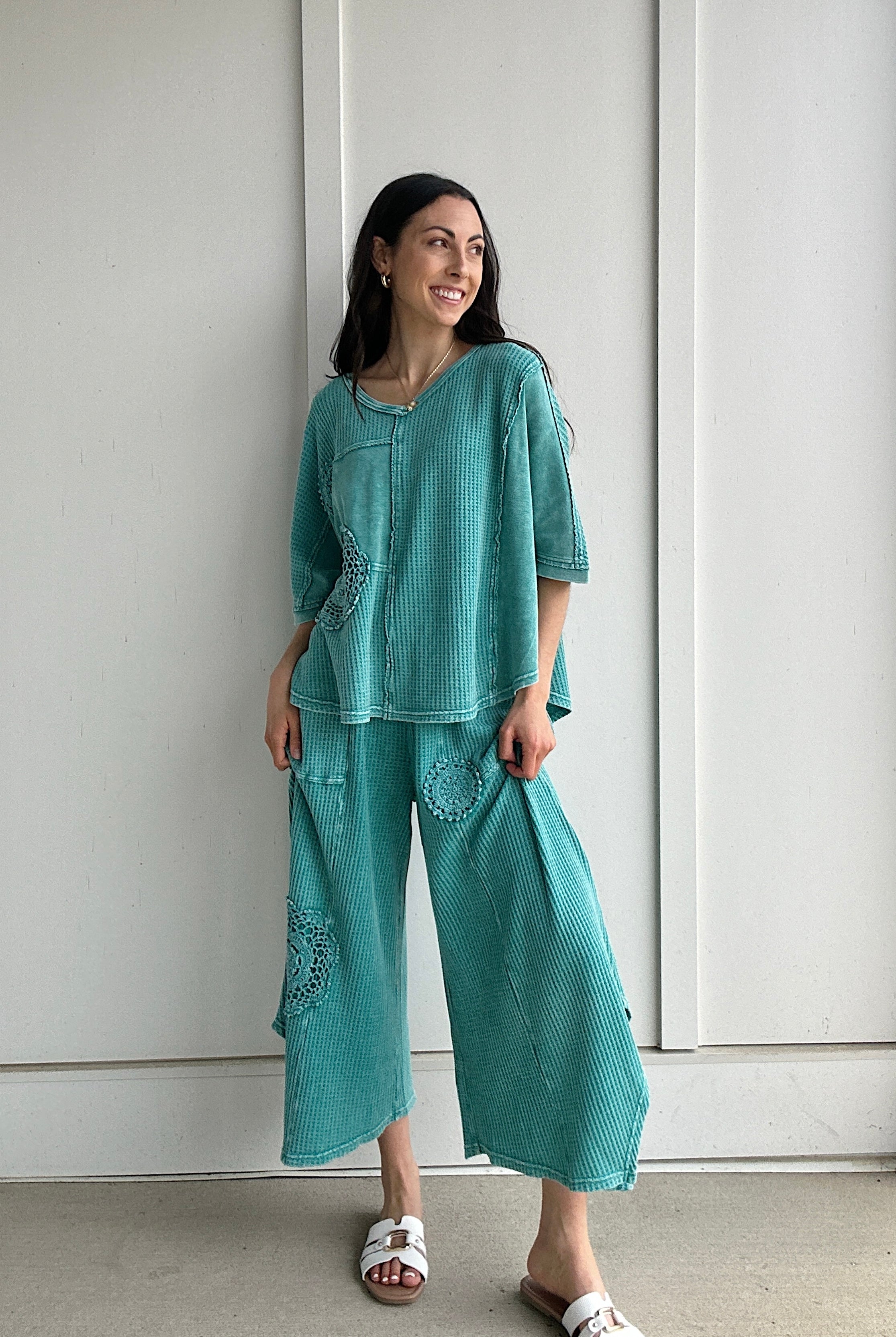 Woman wearing a teal outfit standing against a white wall