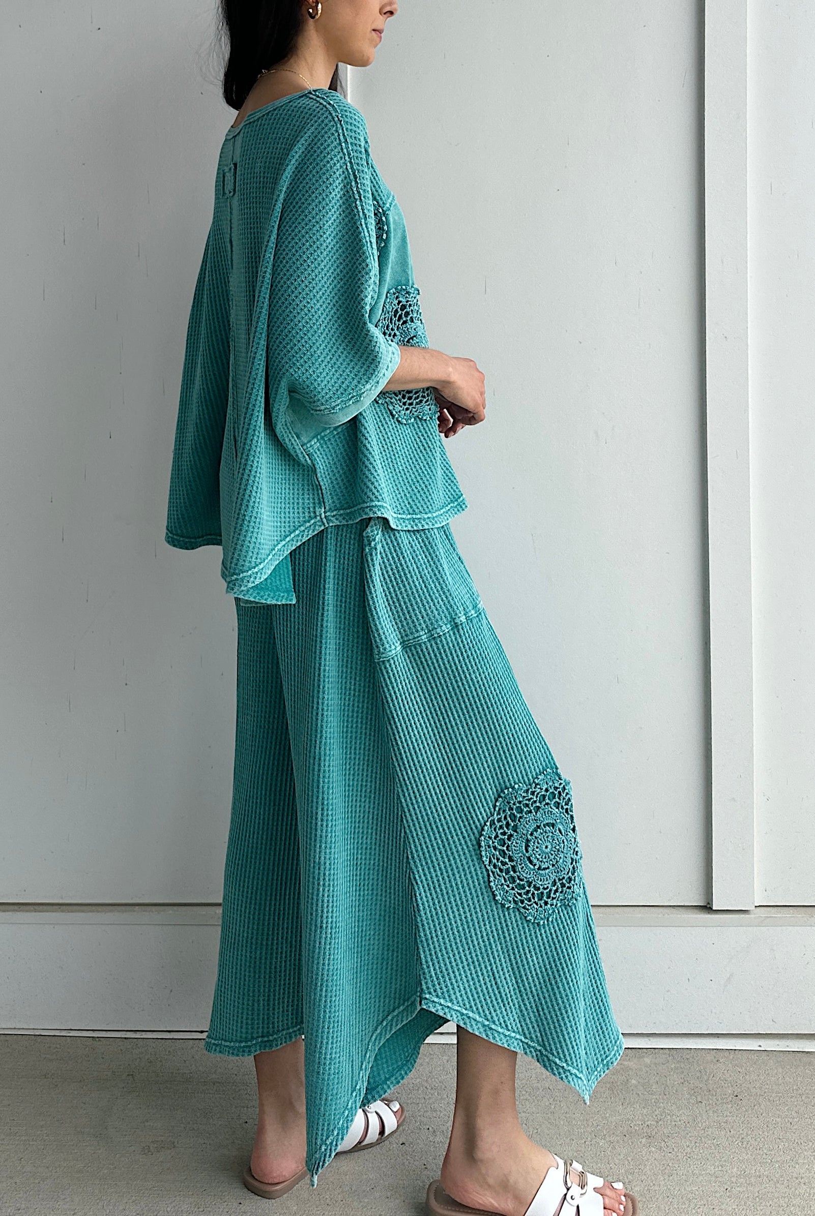 Woman wearing a teal outfit with floral embellishments against a white background showing side