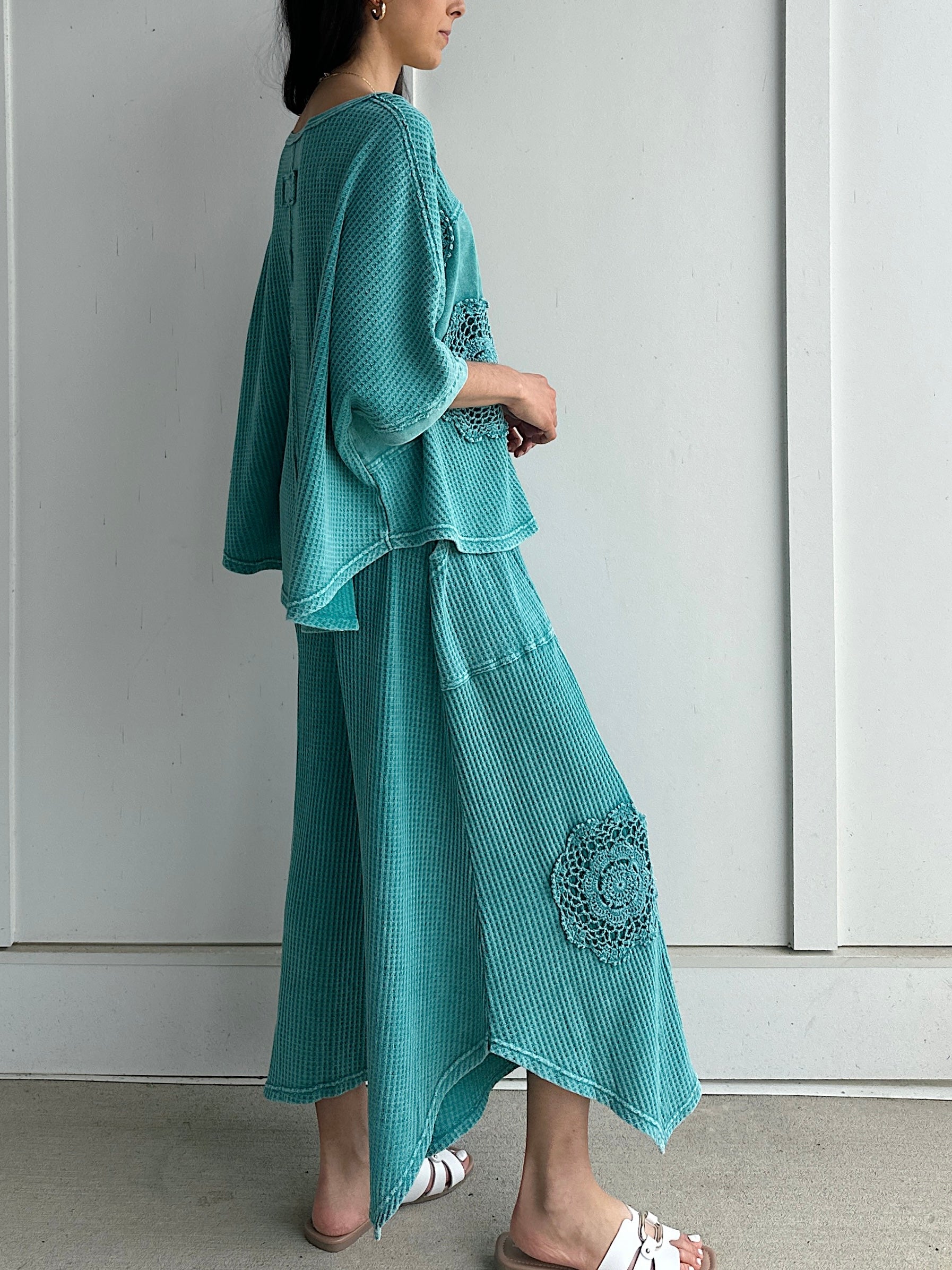 Woman wearing a teal outfit with floral embellishments against a white background showing side