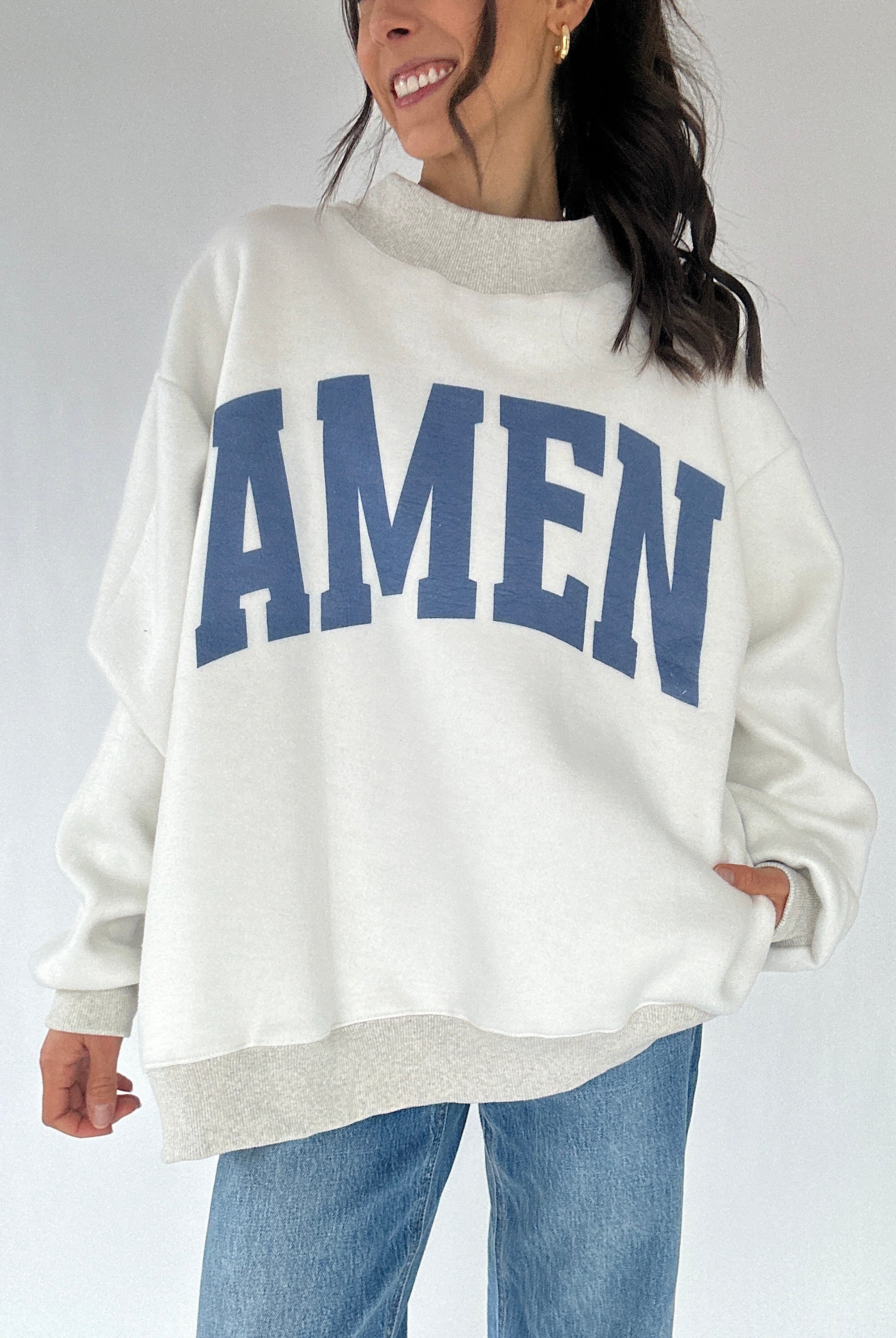 Person wearing a white sweatshirt with 'AMEN' printed in blue on a plain background