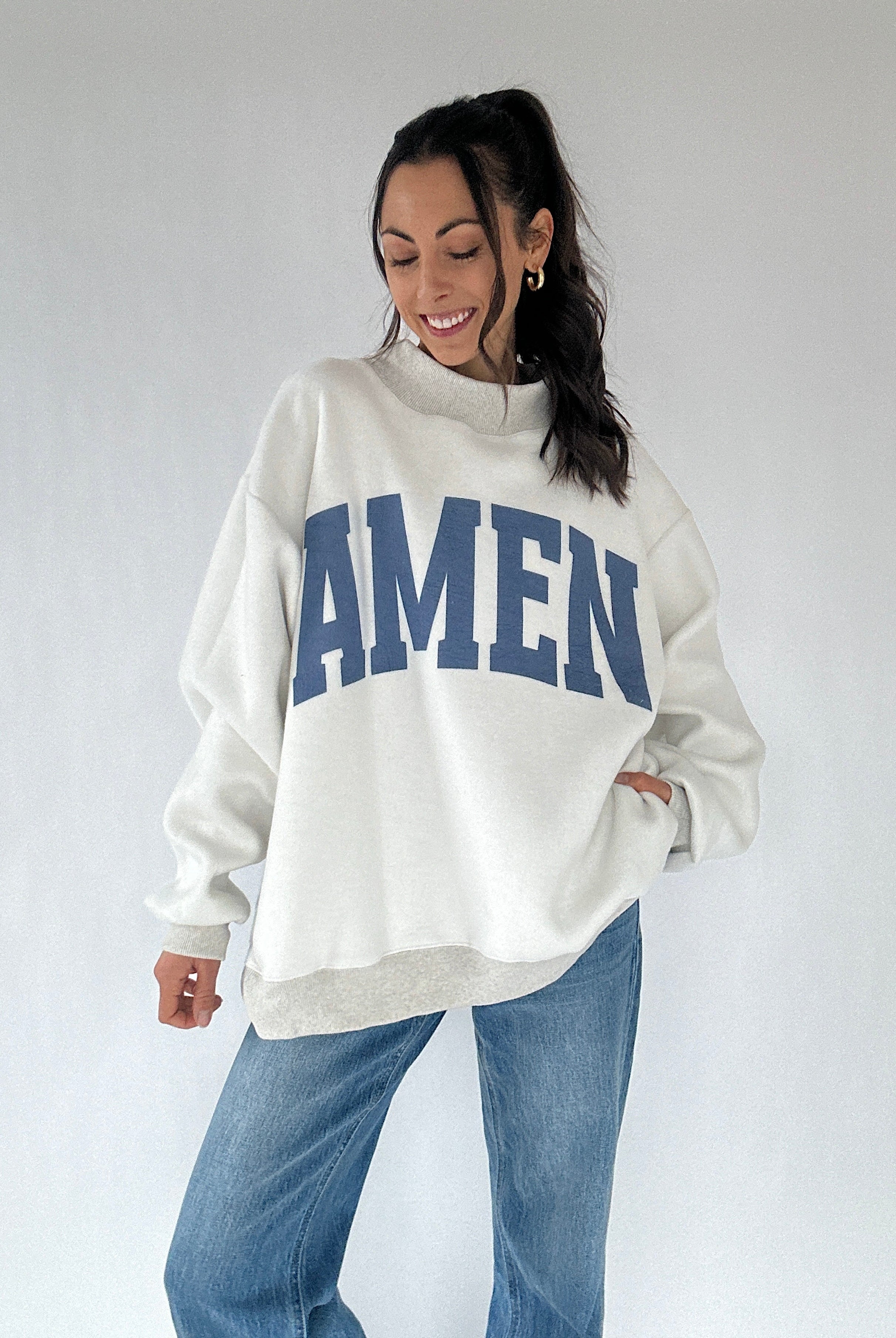 Person wearing a white sweatshirt with 'AMEN' printed in blue on a plain background