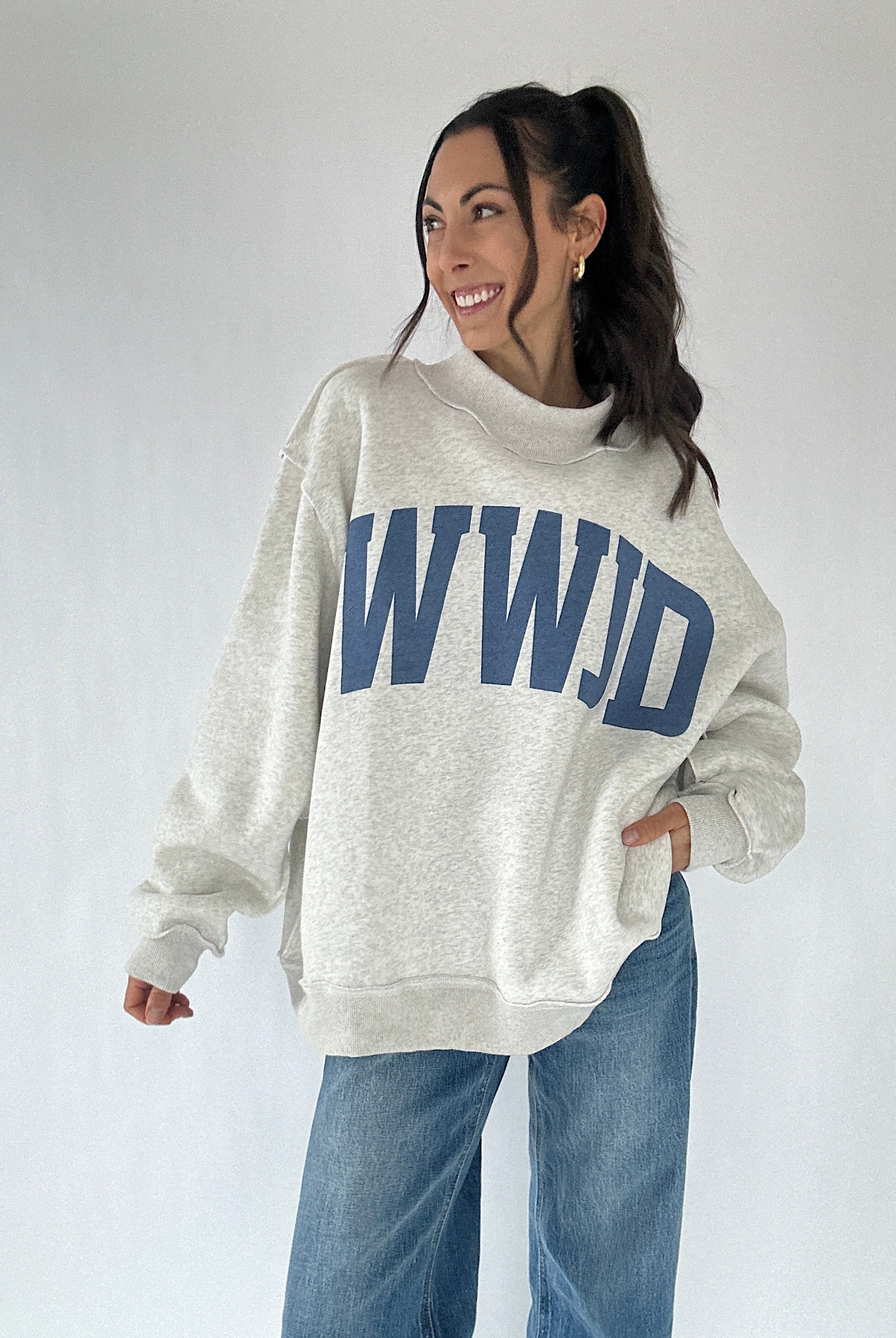 Person wearing a gray mockneck sweatshirt with 'WWJD' printed in blue on a plain background