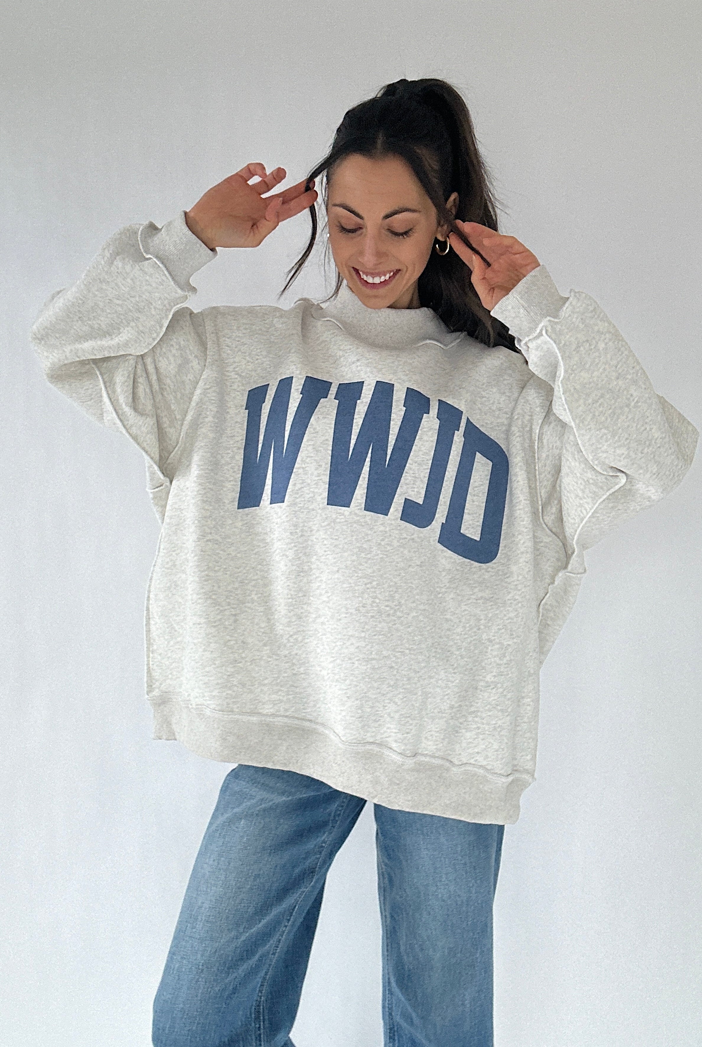 Person wearing a gray sweatshirt with 'WWJD' text on a plain background