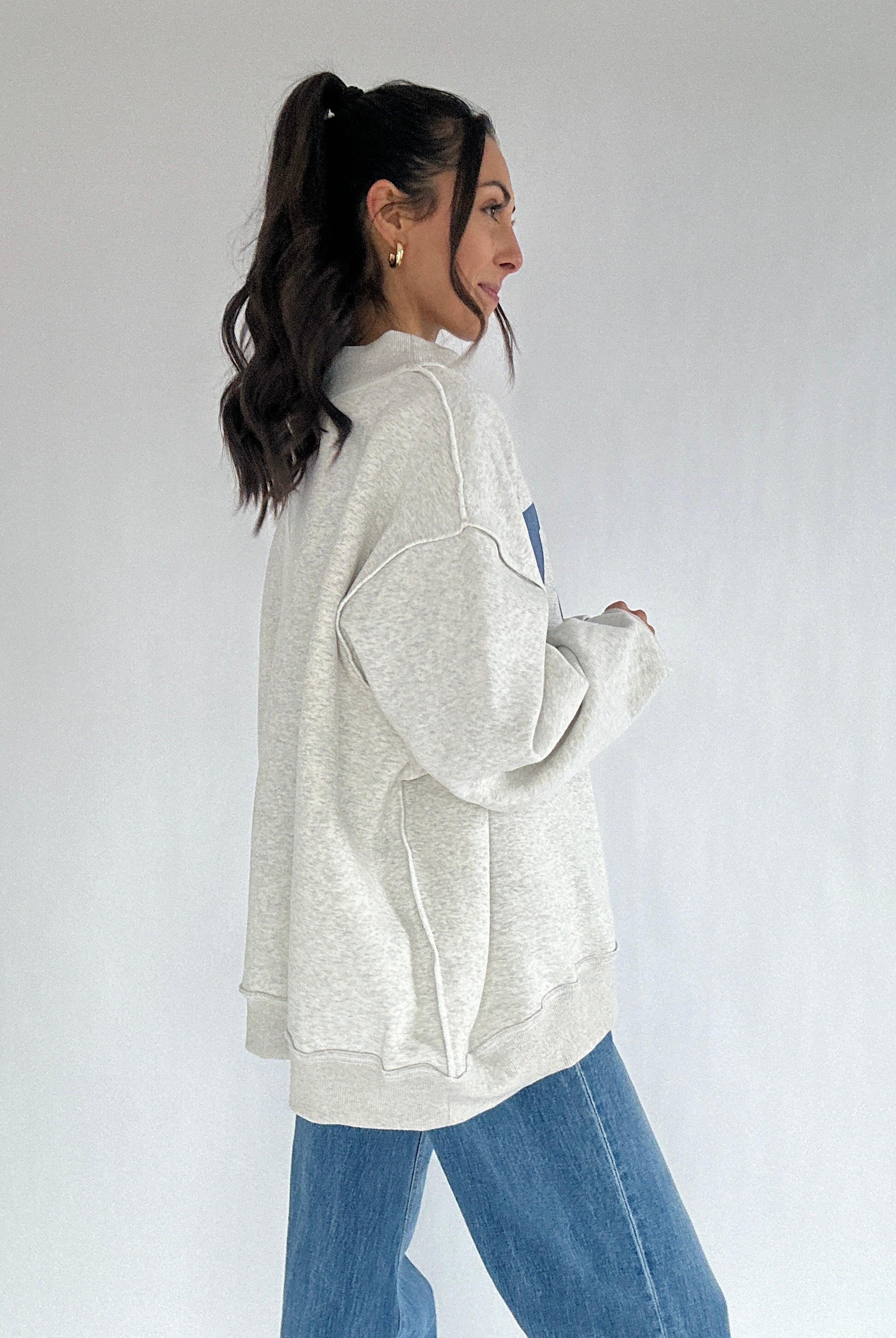 Woman wearing a light gray oversized sweatshirt and blue jeans on a white background from side