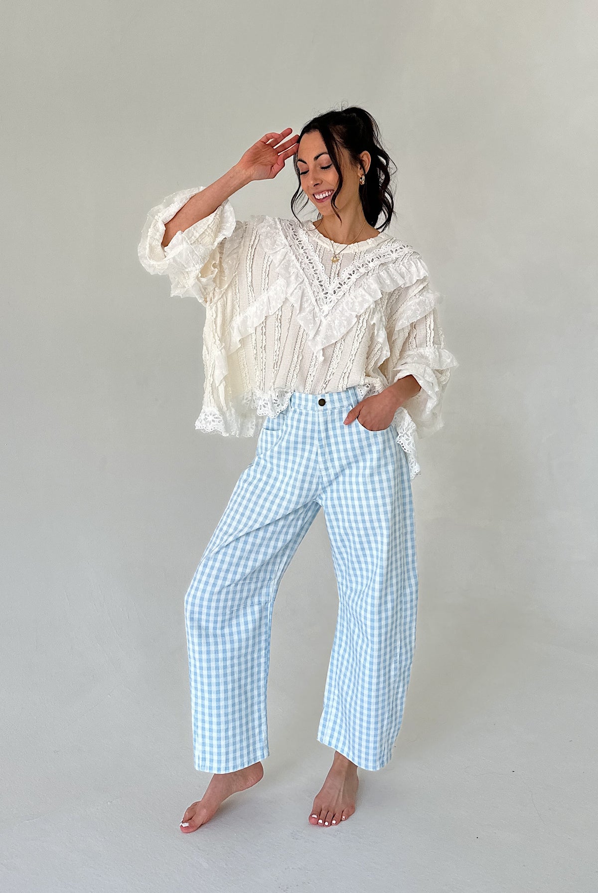 Woman wearing a white lace top and light blue checkered pants against a plain background