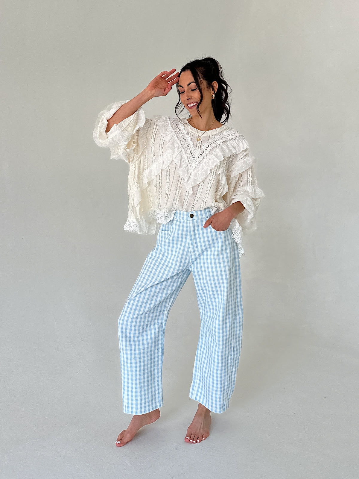 Woman wearing a white lace top and light blue checkered pants against a plain background