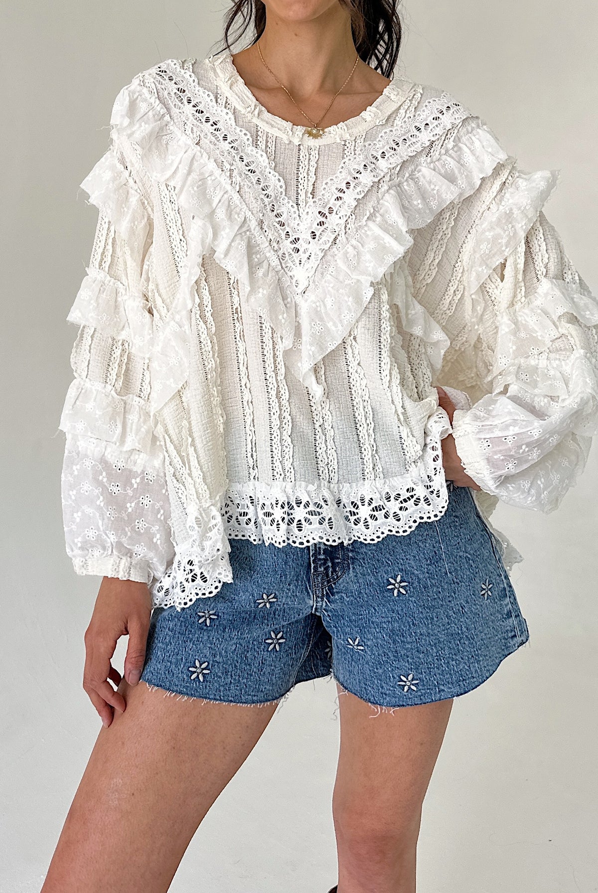 Person wearing a white lace blouse and denim shorts on a plain background