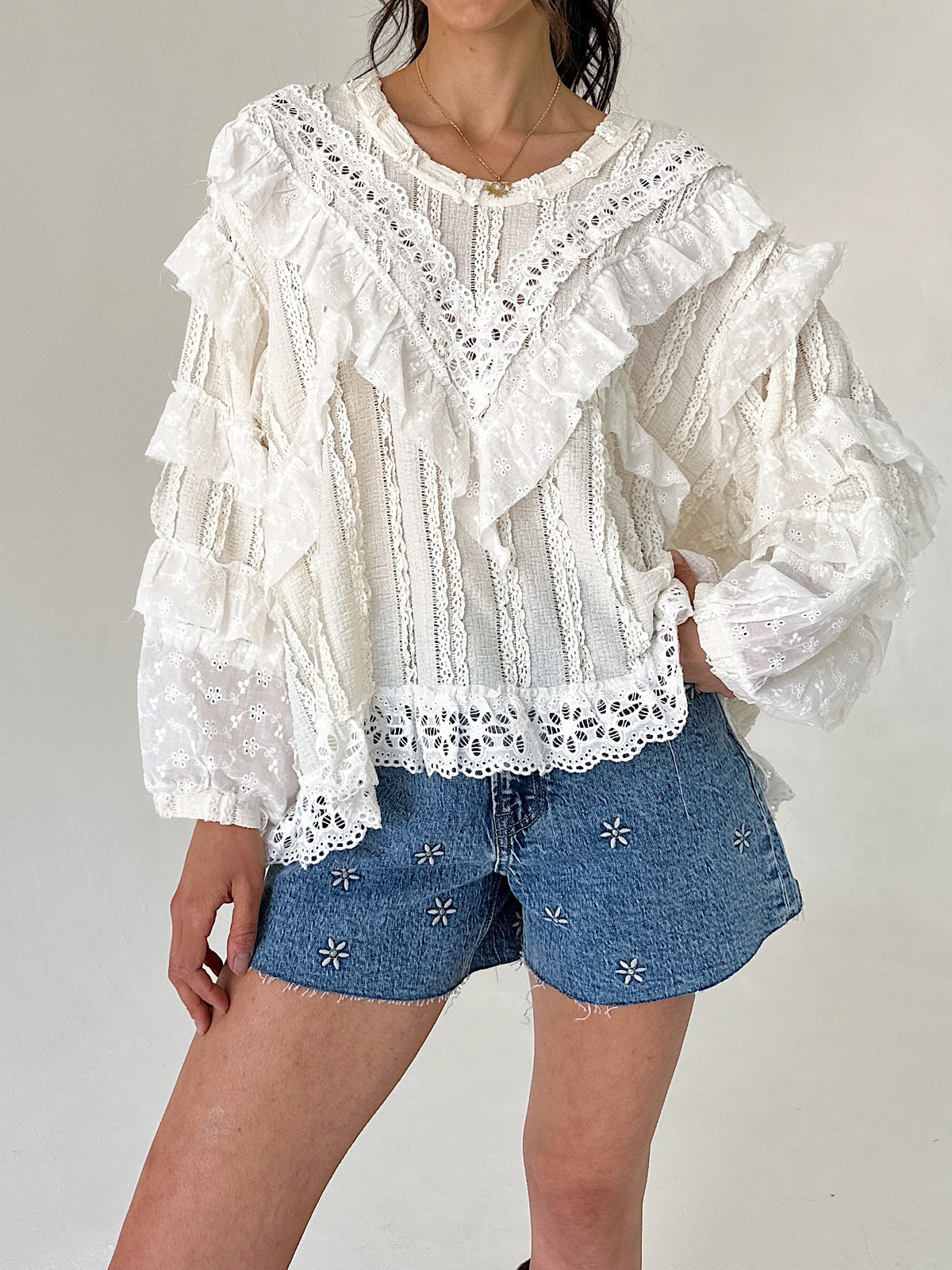 Person wearing a white lace blouse and denim shorts on a plain background